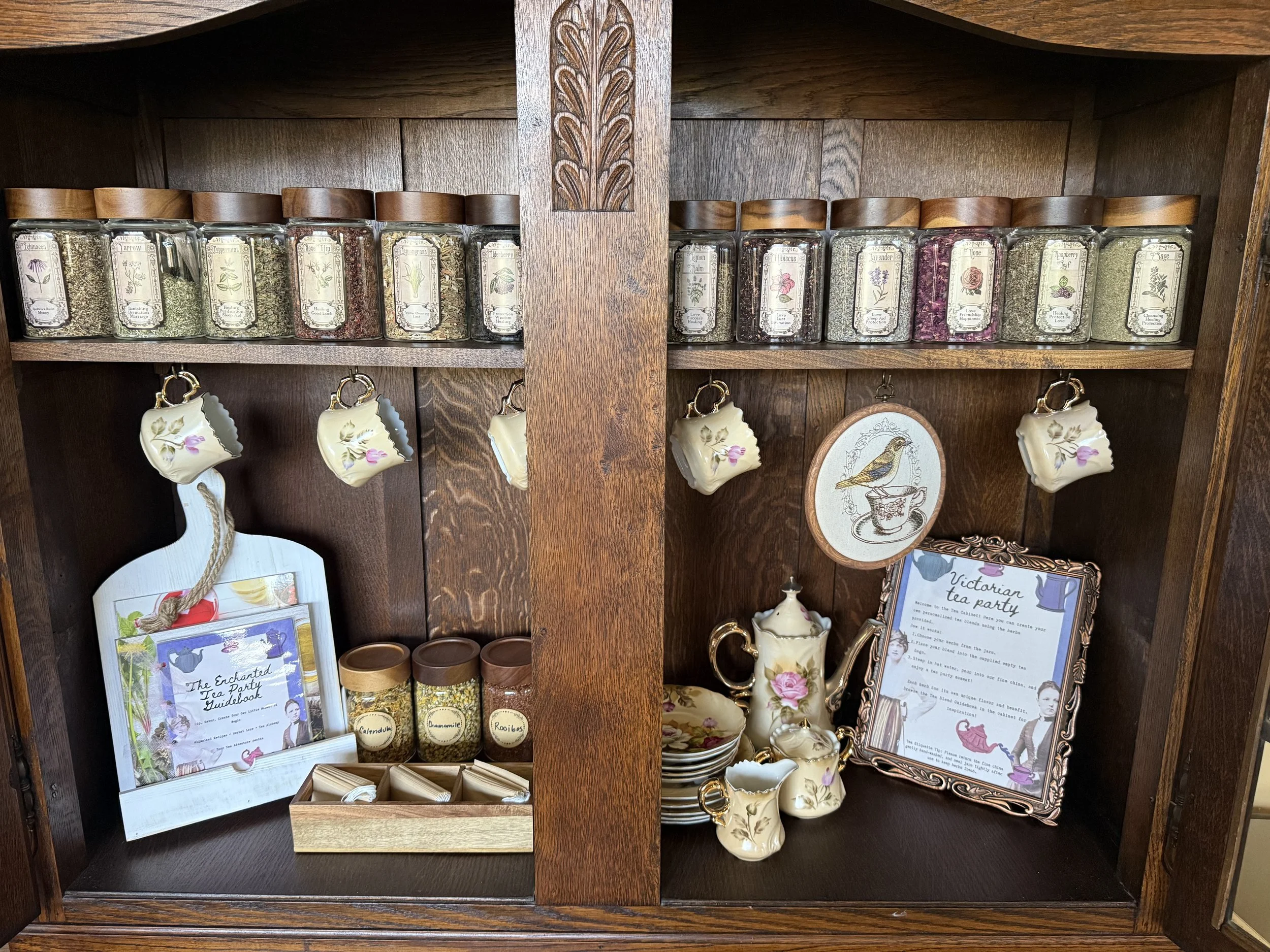 Wooden cabinet with glass jars of dried tea leaves, teacups, teapot, and framed signs for a tea party themed event.