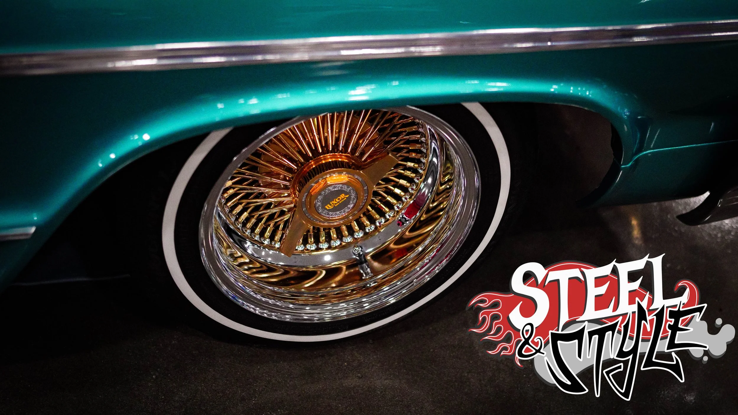 Close-up of a vintage car wheel with a shiny bronze and chrome wire-spoke rim and black wall tire, with a teal-colored car body above and a "Steel & Style" logo on the bottom right.
