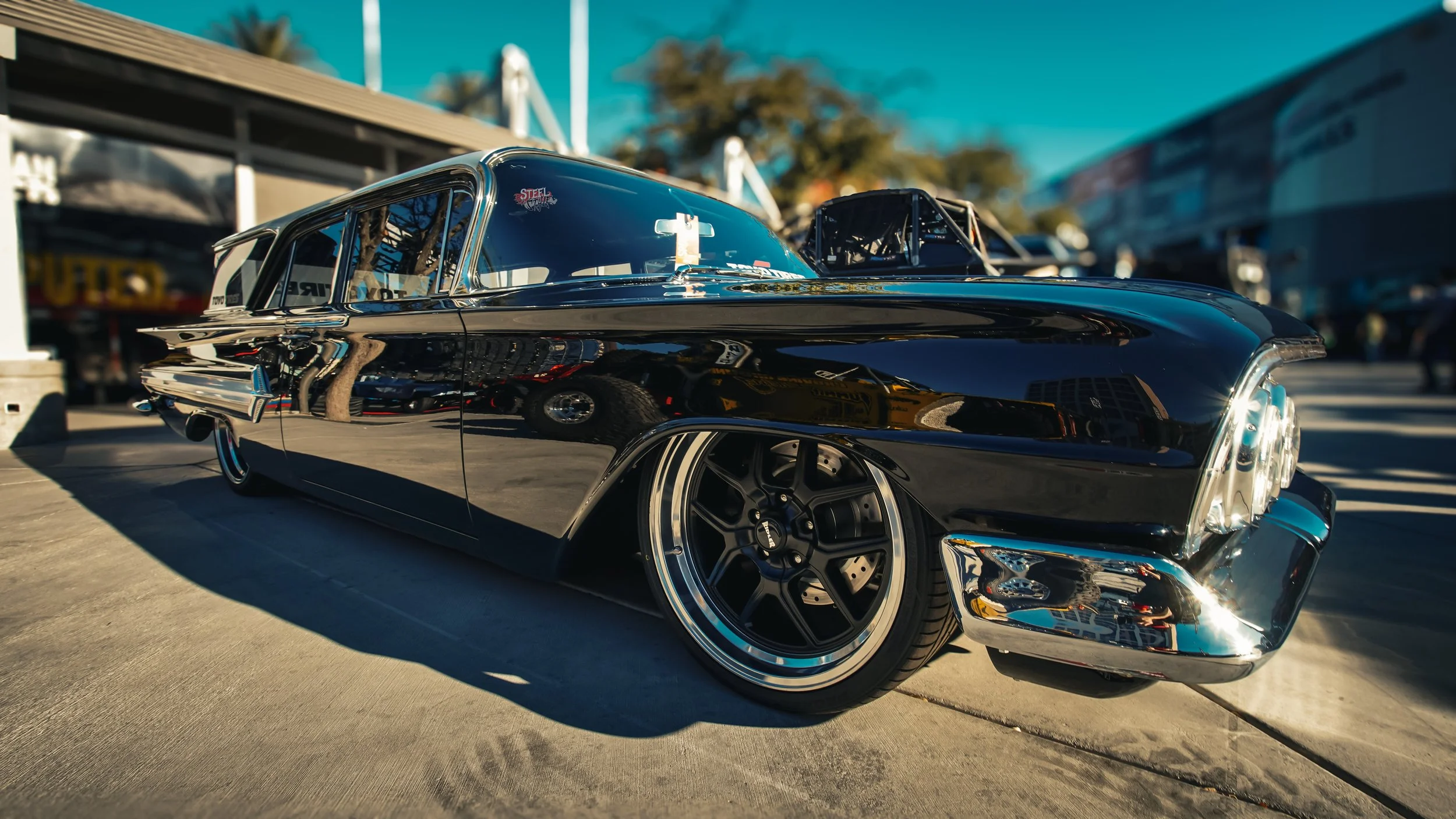 Side view of a black vintage lowrider car with chrome accents, parked at a car show on a sunny day.