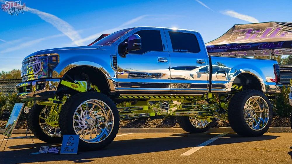 A shiny, highly customized, lifted truck with large wheels and chrome details on display at a car show.