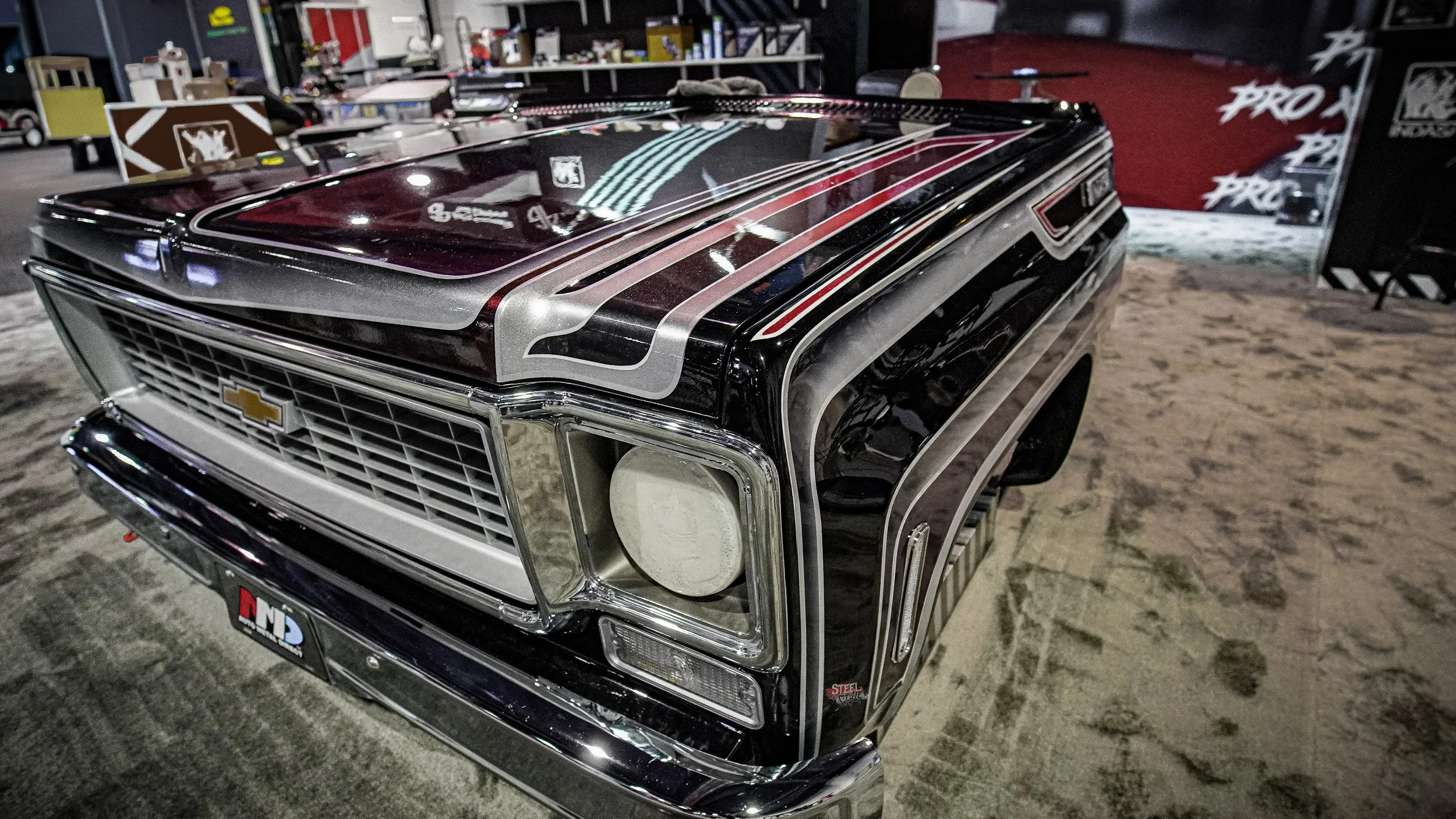 A vintage Chevrolet car with a custom black and silver paint job on display indoors, surrounded by various equipment and displays.