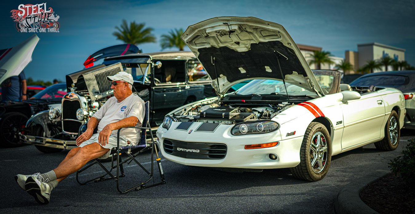 Elderly man sitting beside his late 90's model Camaro