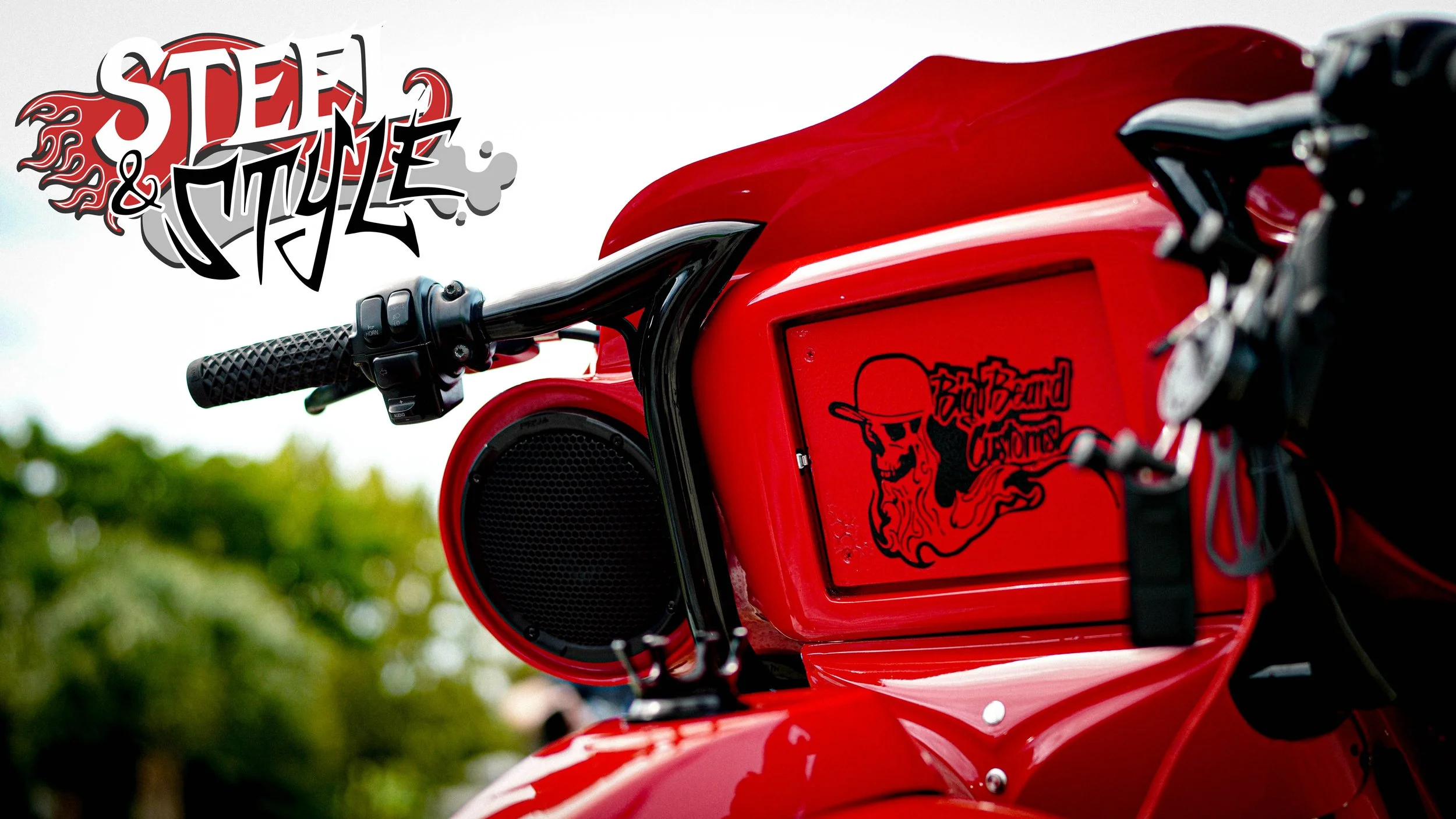 Close-up of a red motorcycle with a sticker saying 'Bad Band of Crum' and a cartoonish skeleton wearing a hat. The background shows trees and a cloudy sky.