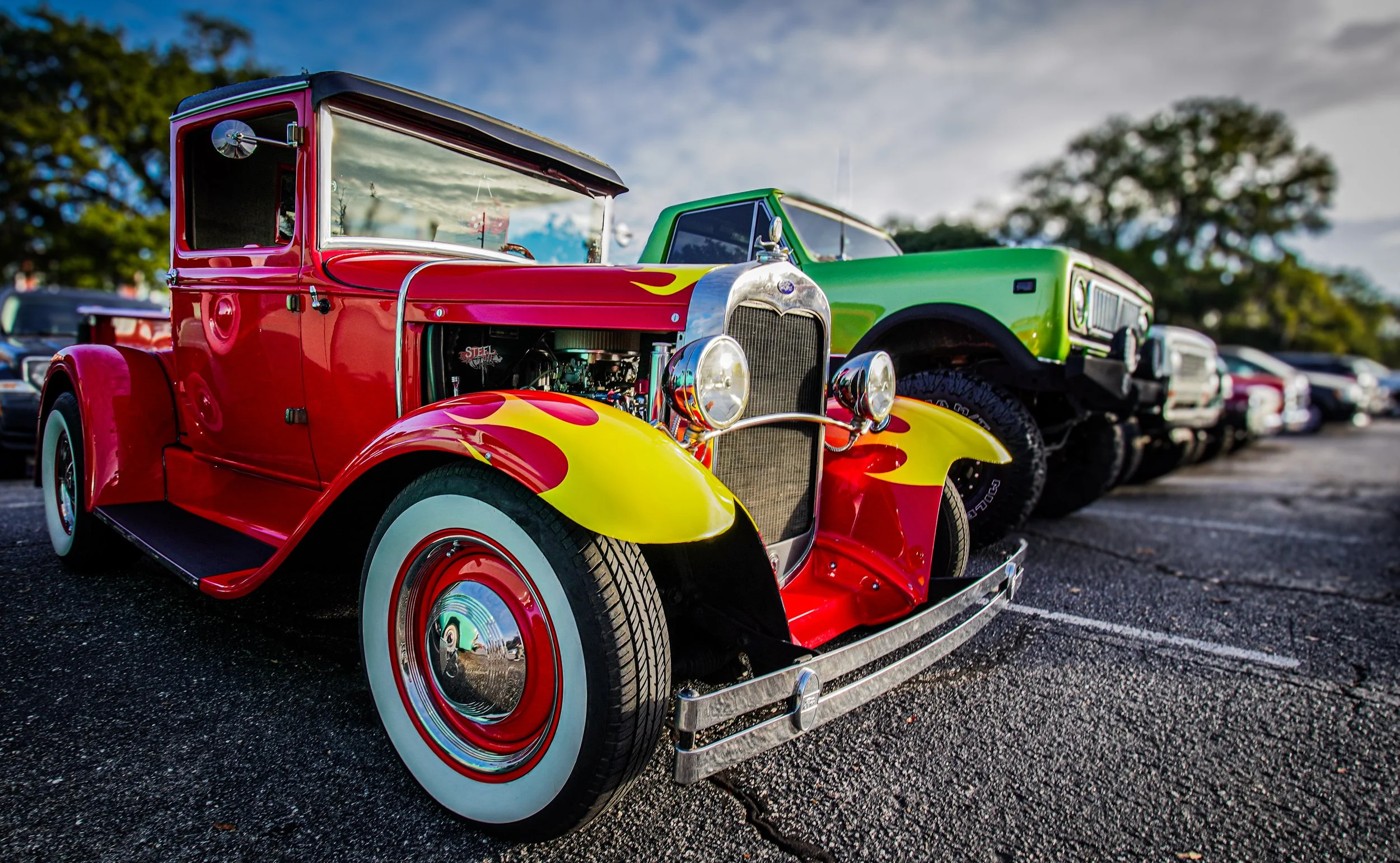 Colorful vintage cars parked in a row at a car show, with a prominent red and yellow classic car in the foreground.