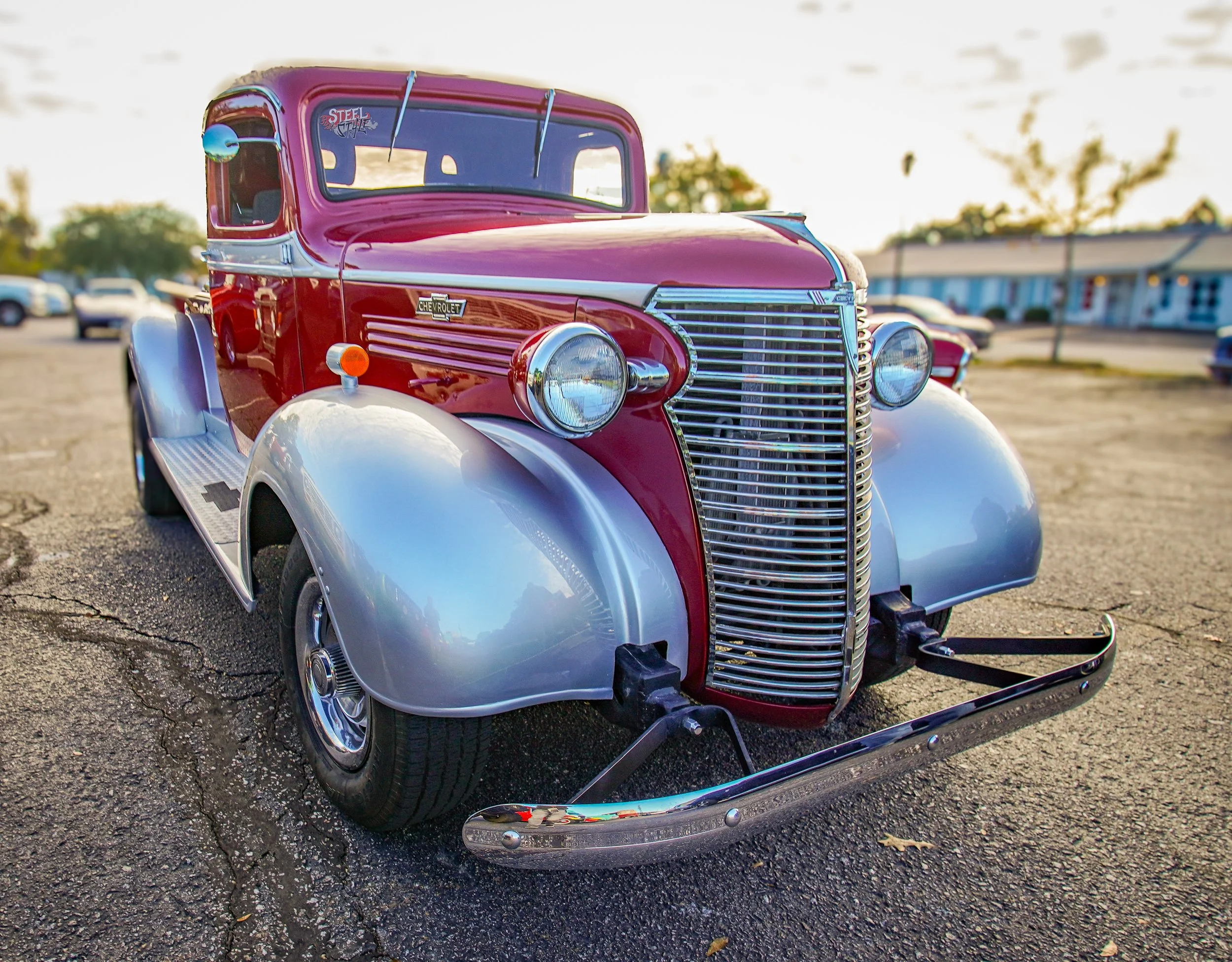 A vintage red and silver Chevrolet truck parked on an asphalt lot during sunset.