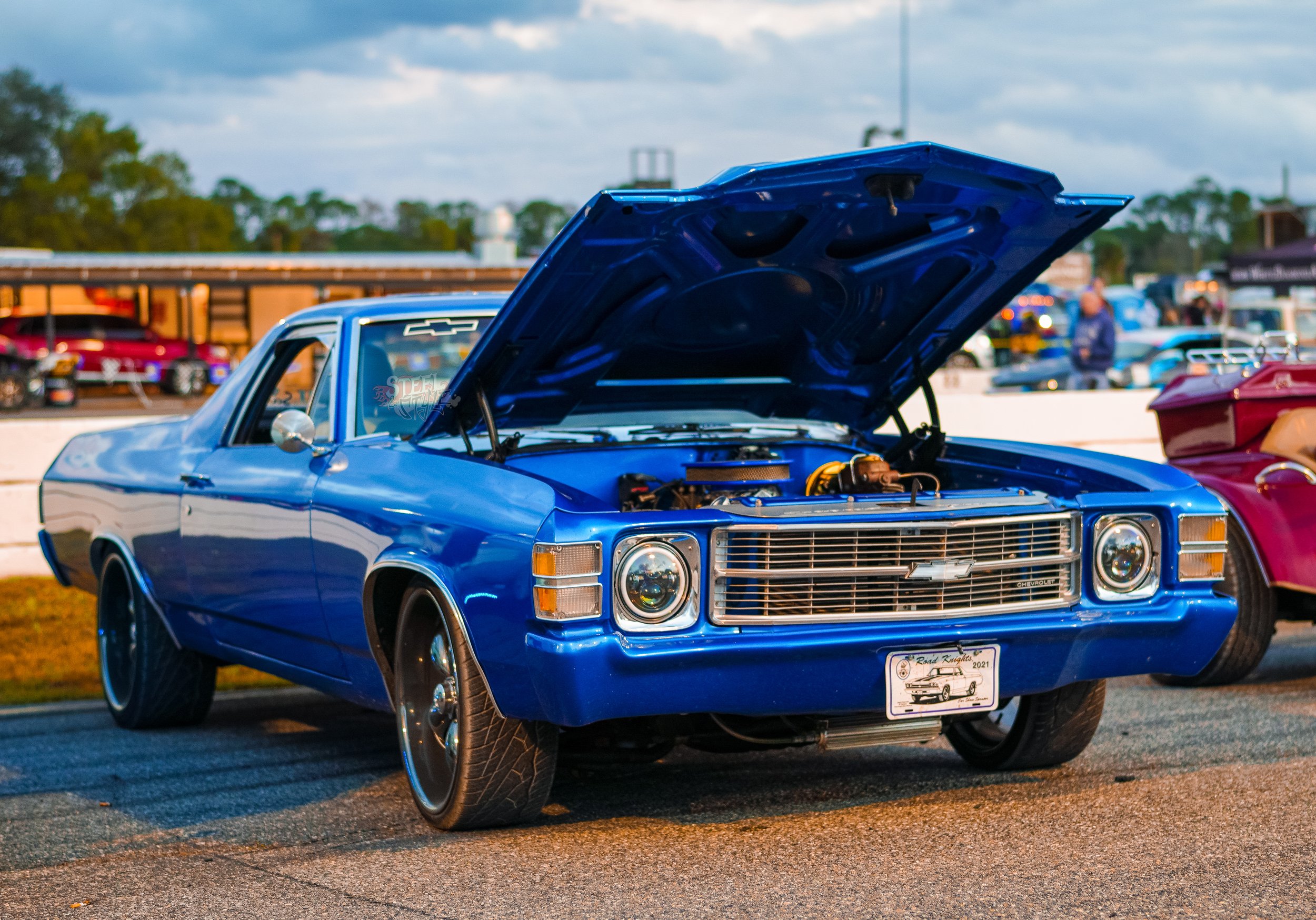 A classic blue Chevrolet muscle car with its hood open, displayed at a car show.