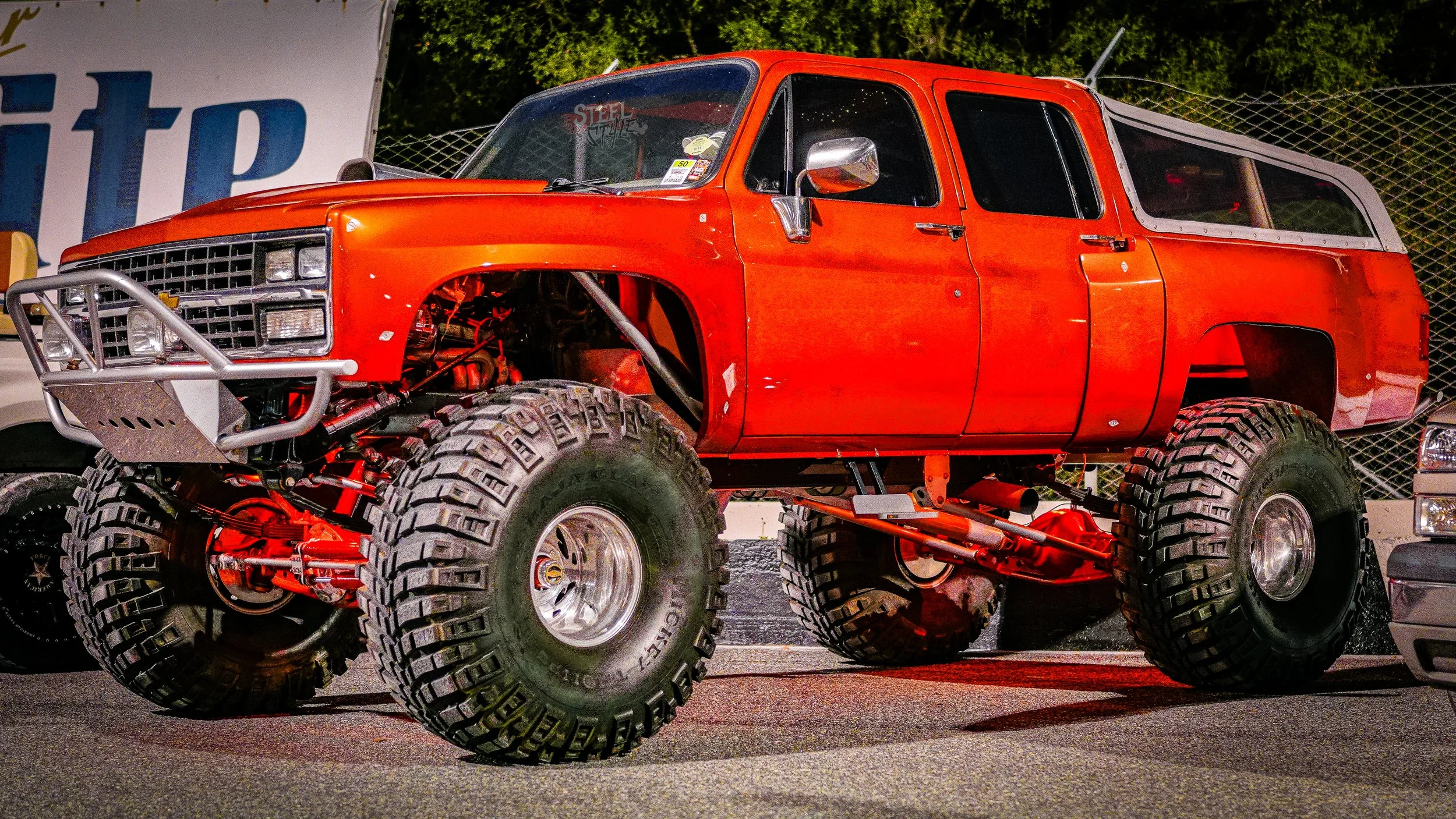 A large red off-road monster truck with oversized tires parked on asphalt at night.