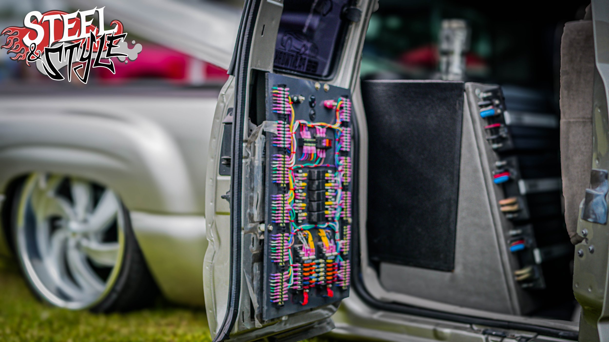 Open door of a classic car showing its complex wiring and relay setup.