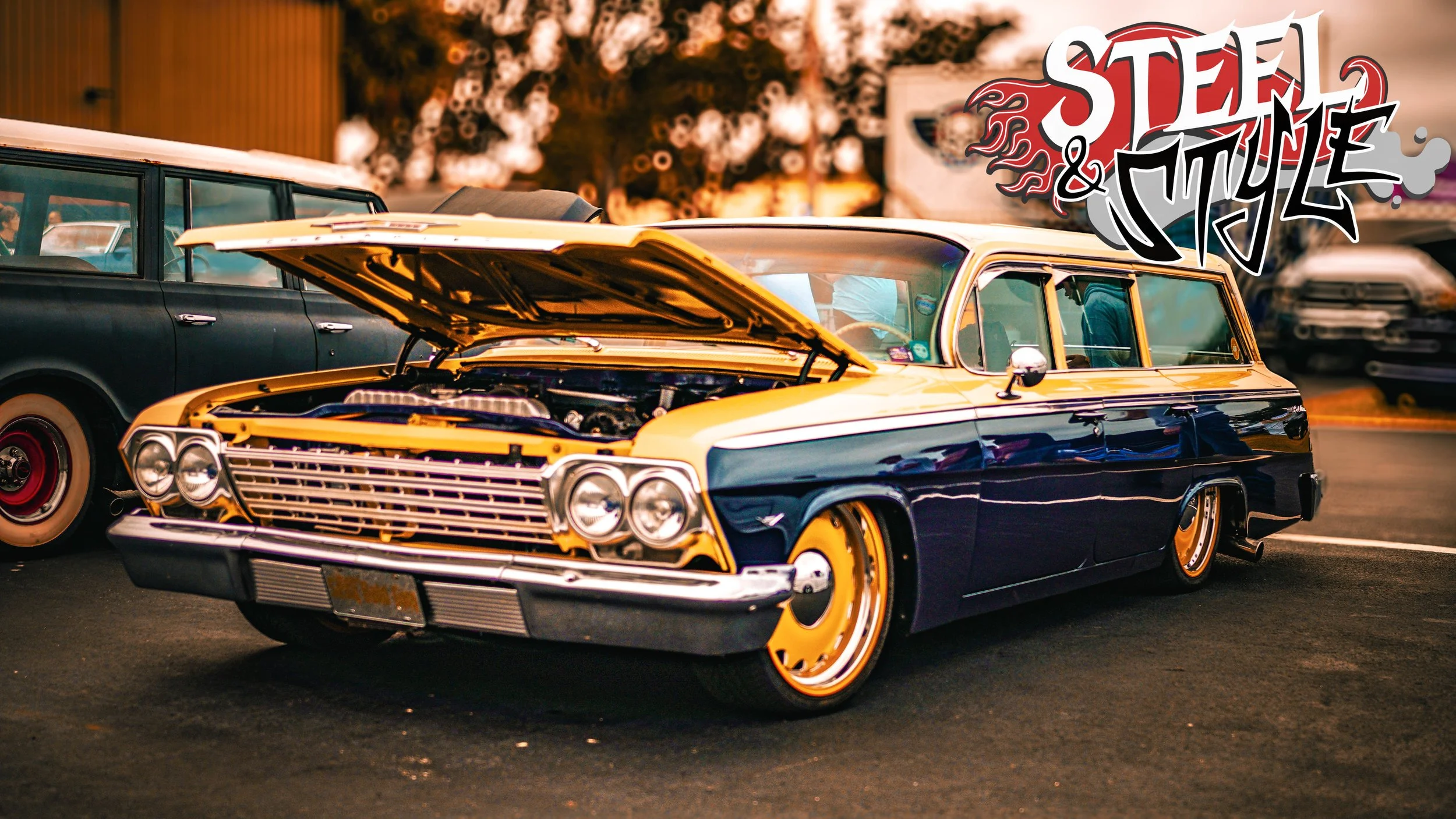 A vintage yellow and black station wagon with its hood open parked at a car show, with other classic cars in the background and "Steel & Style" graffiti-style text in the upper right corner.