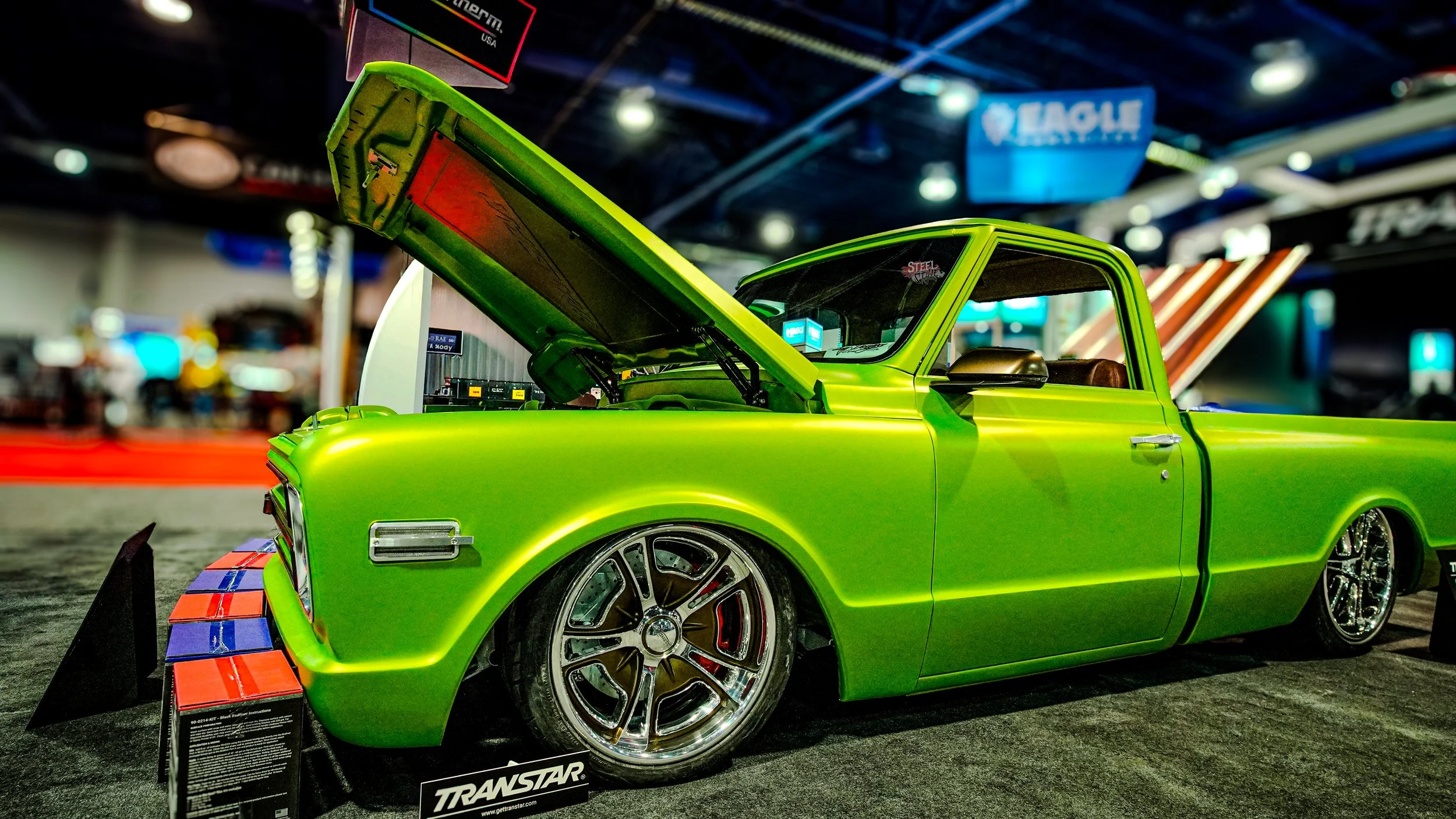 A lime green custom pickup truck displayed at an indoor car show with its hood open, showcasing the engine.