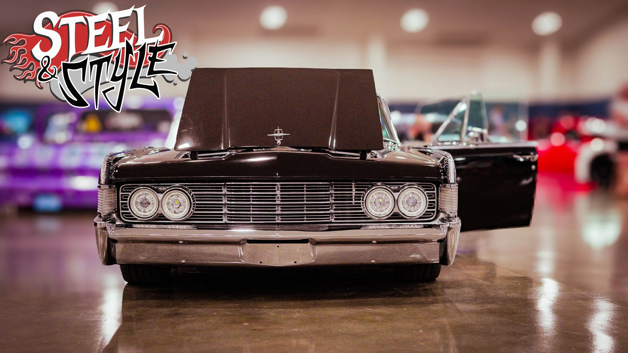 A vintage black-scale model car on display, with the front facing forward and the driver's side door open, at an indoor exhibition with other cars in the background.