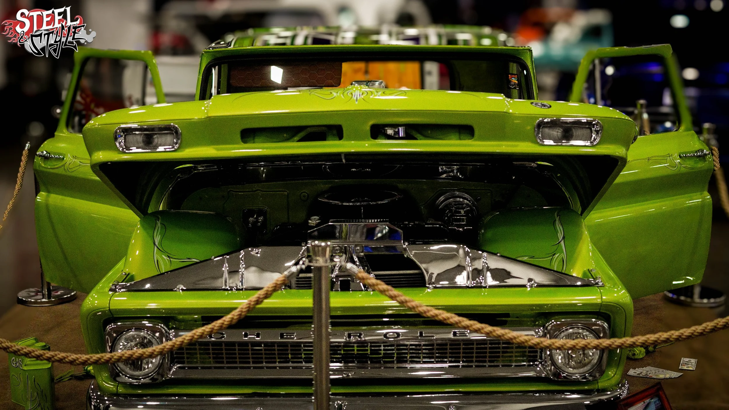 A bright green classic Chevrolet car on display with its hood open, showing the engine inside, at a car show or exhibition.