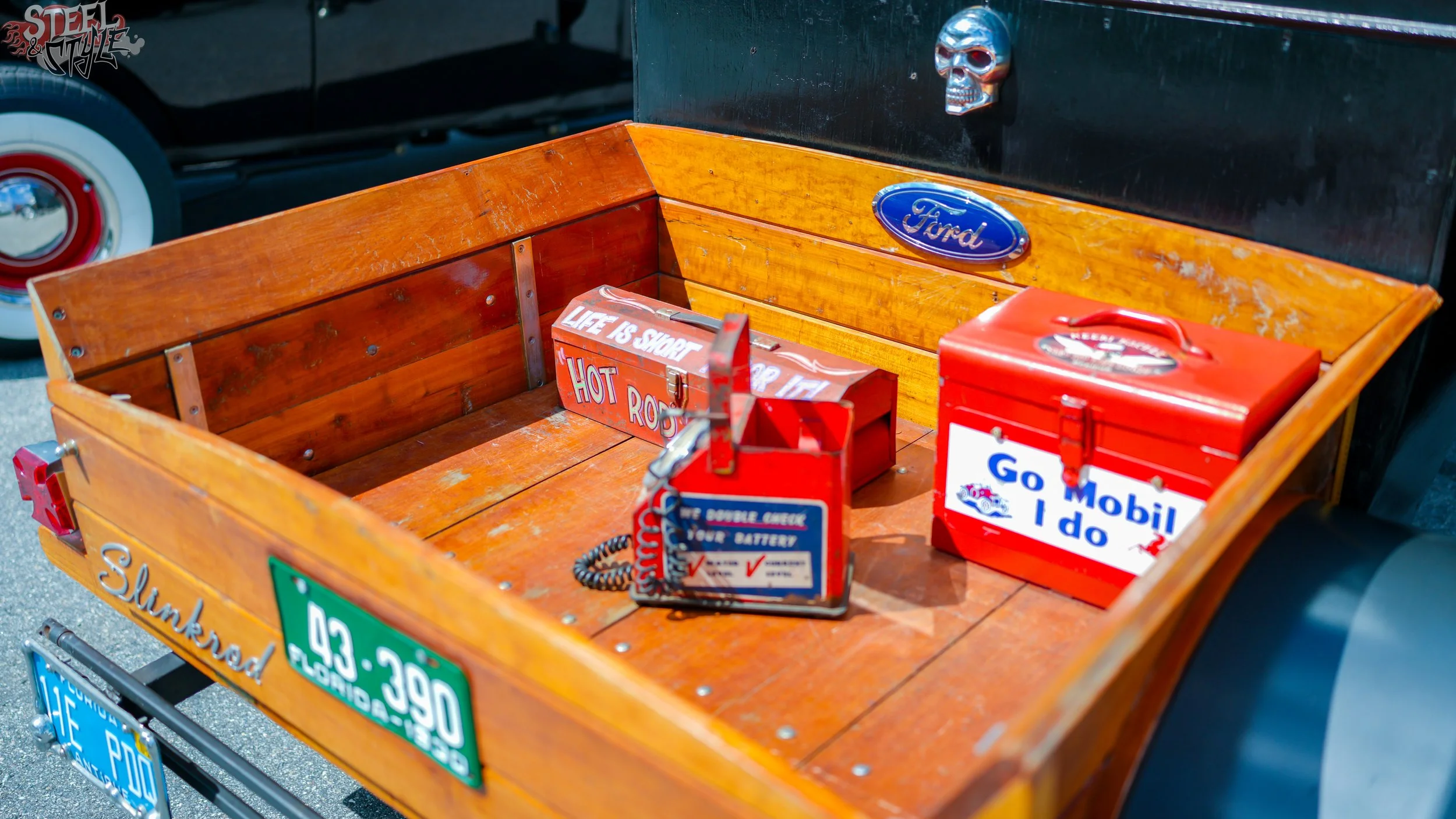 A wooden car trunk with vintage signs and boxes, featuring a skull ornament on a black background.