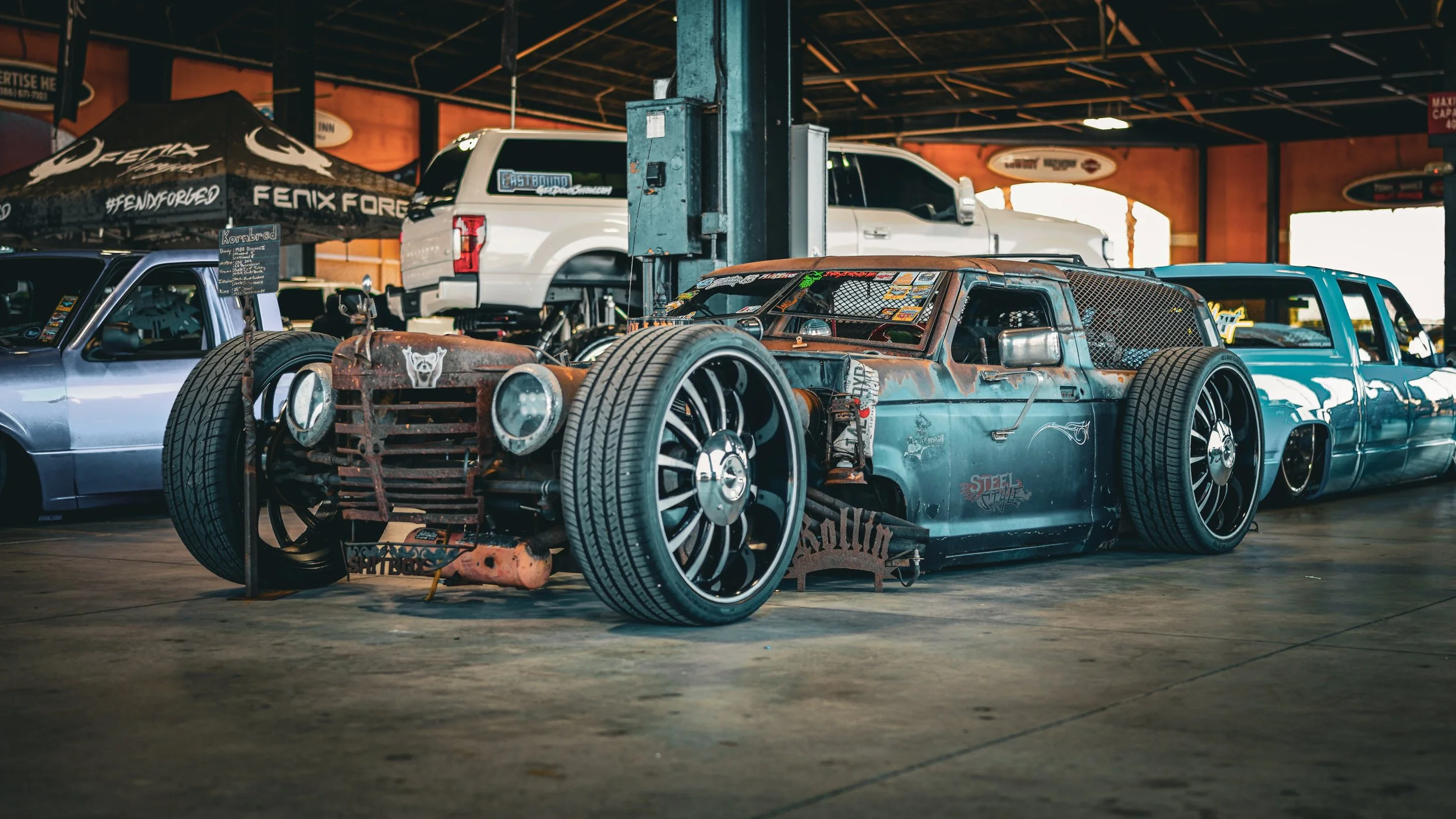 A rusty, custom-built heat car with large wheels and a chopper-style body design, displayed indoors at a car show.