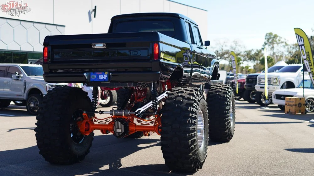 Black lifted truck with oversized tires displayed outdoors at an auto show.
