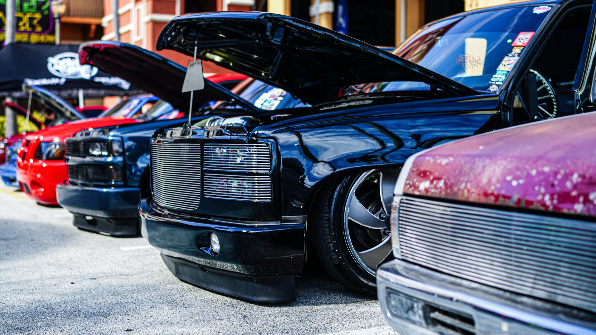 Row of vintage cars on display at a car show, with hoods open, showcasing their engines and modifications.