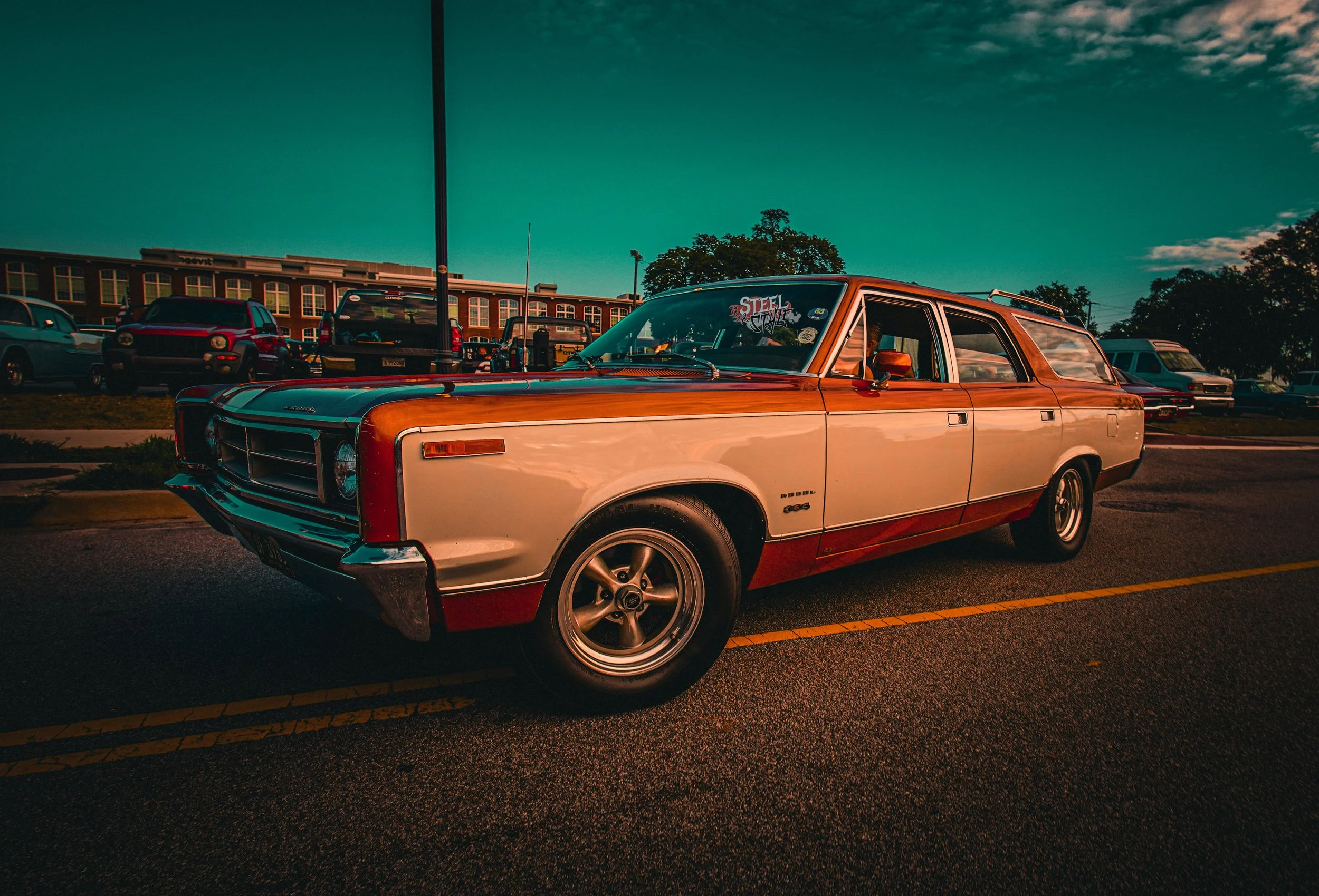 A vintage station wagon parked in a parking lot during sunset with a building and several other cars in the background.