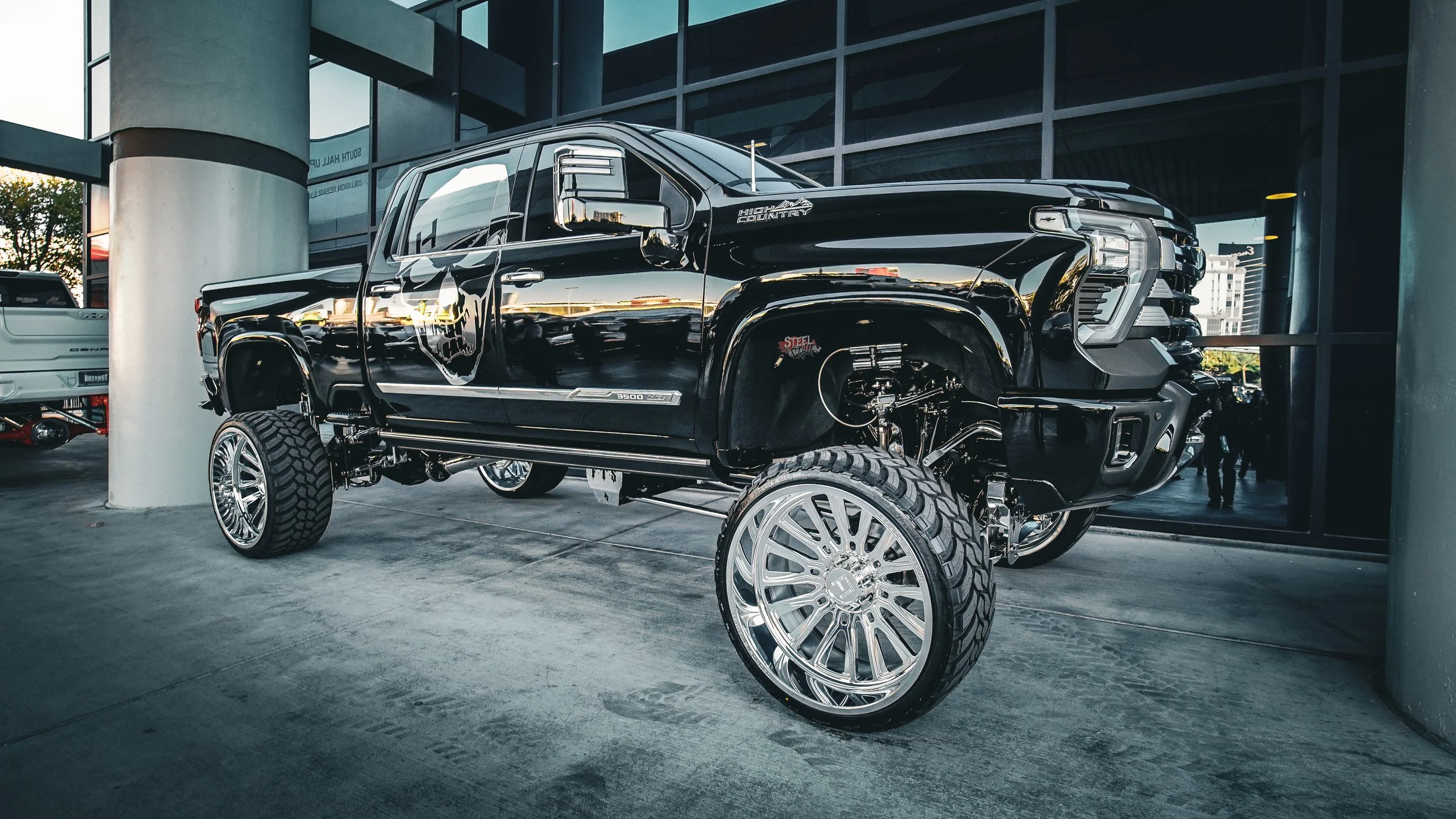 A black lifted pickup truck with chrome wheels parked outside a building.
