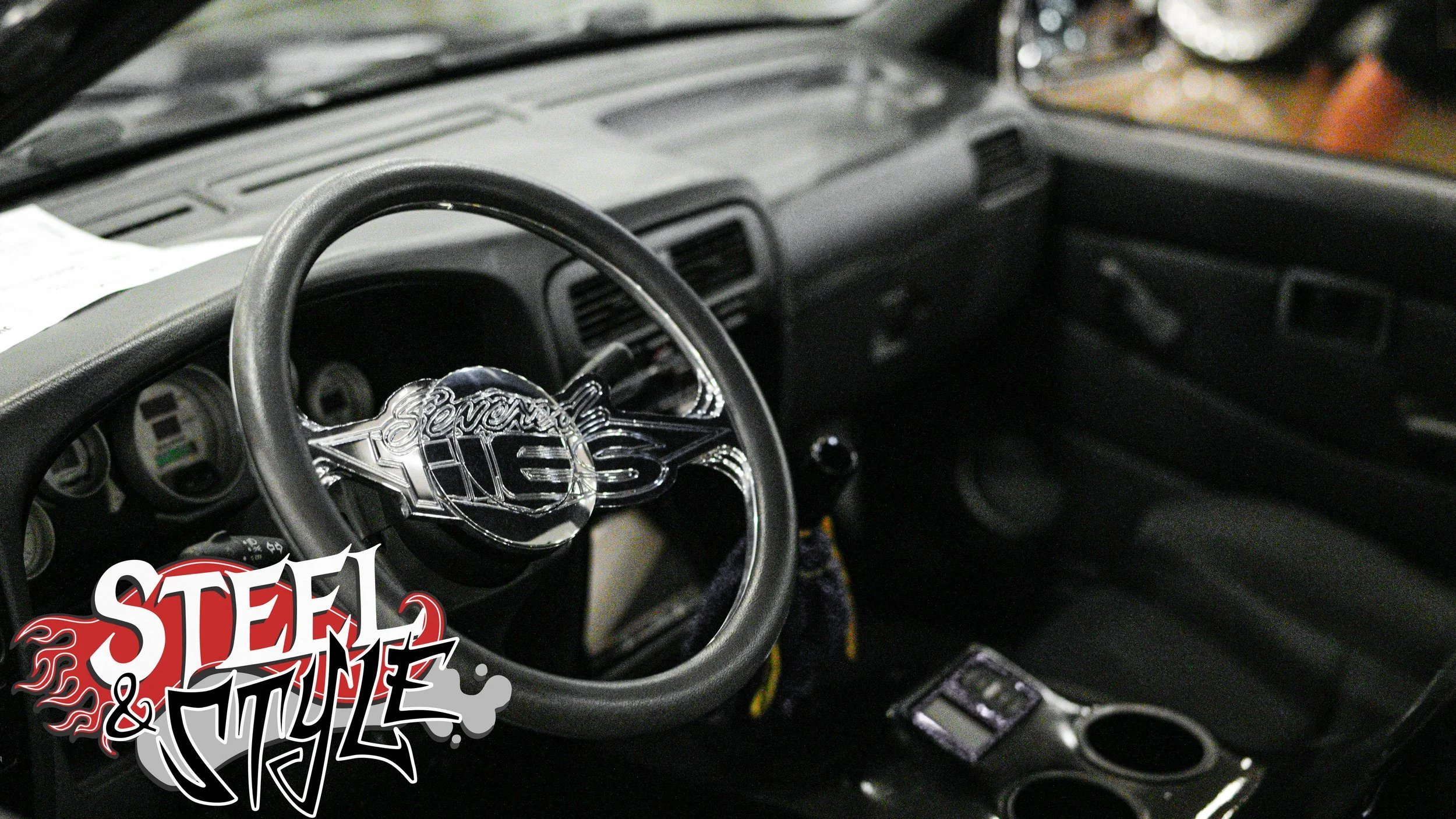 Interior of a vehicle with a steering wheel featuring a large chrome emblem, dashboard, and center console.