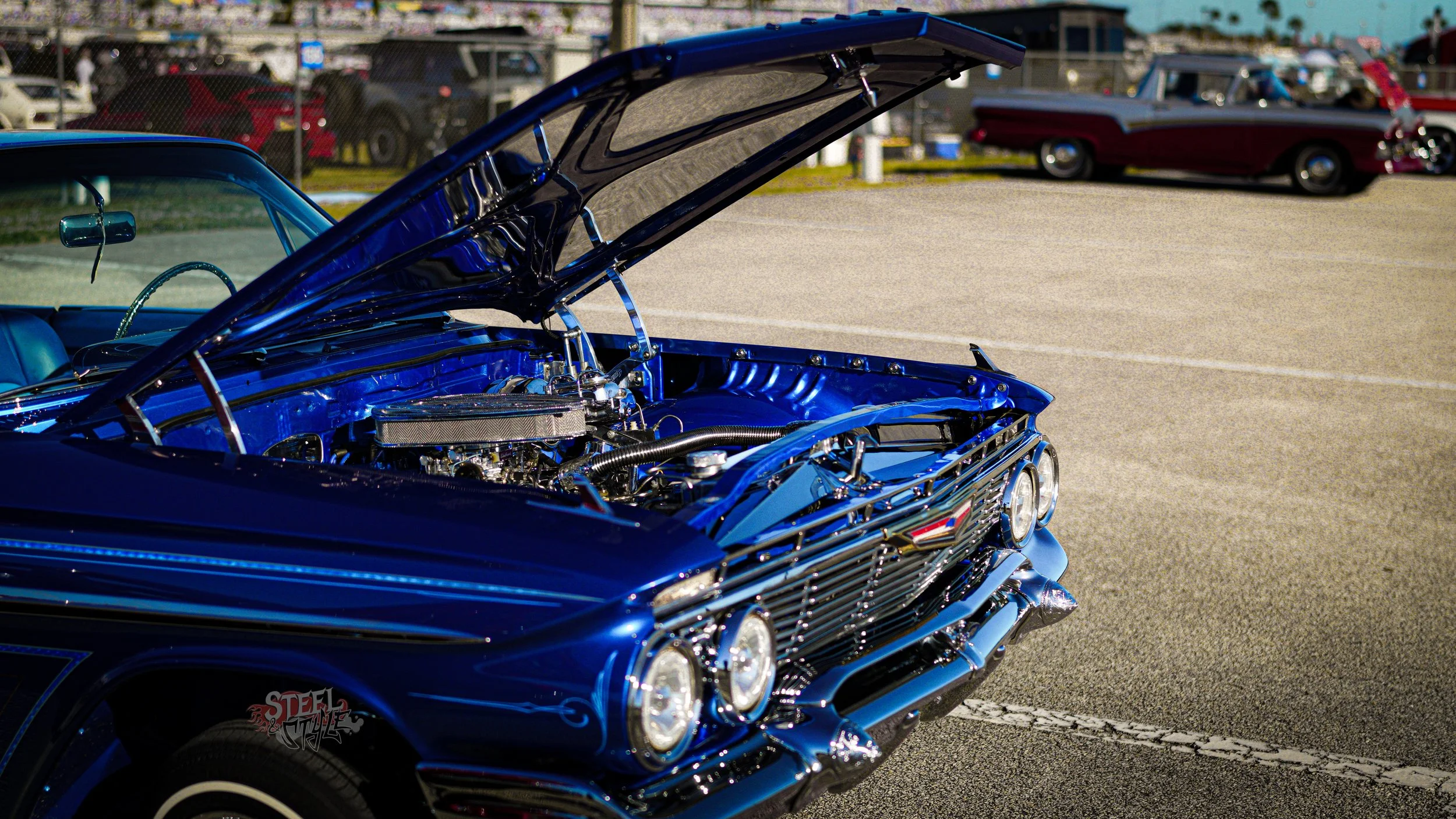A classic blue car with its hood open at a car show.