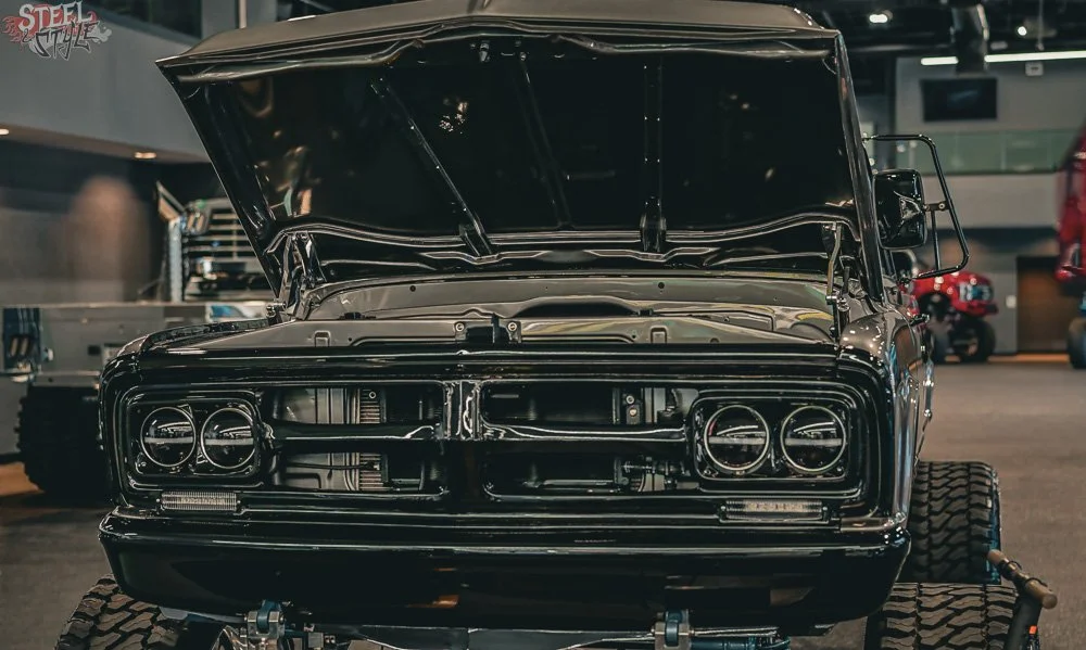 A black vintage muscle car with its hood open on display at a car show, showing its engine compartment.