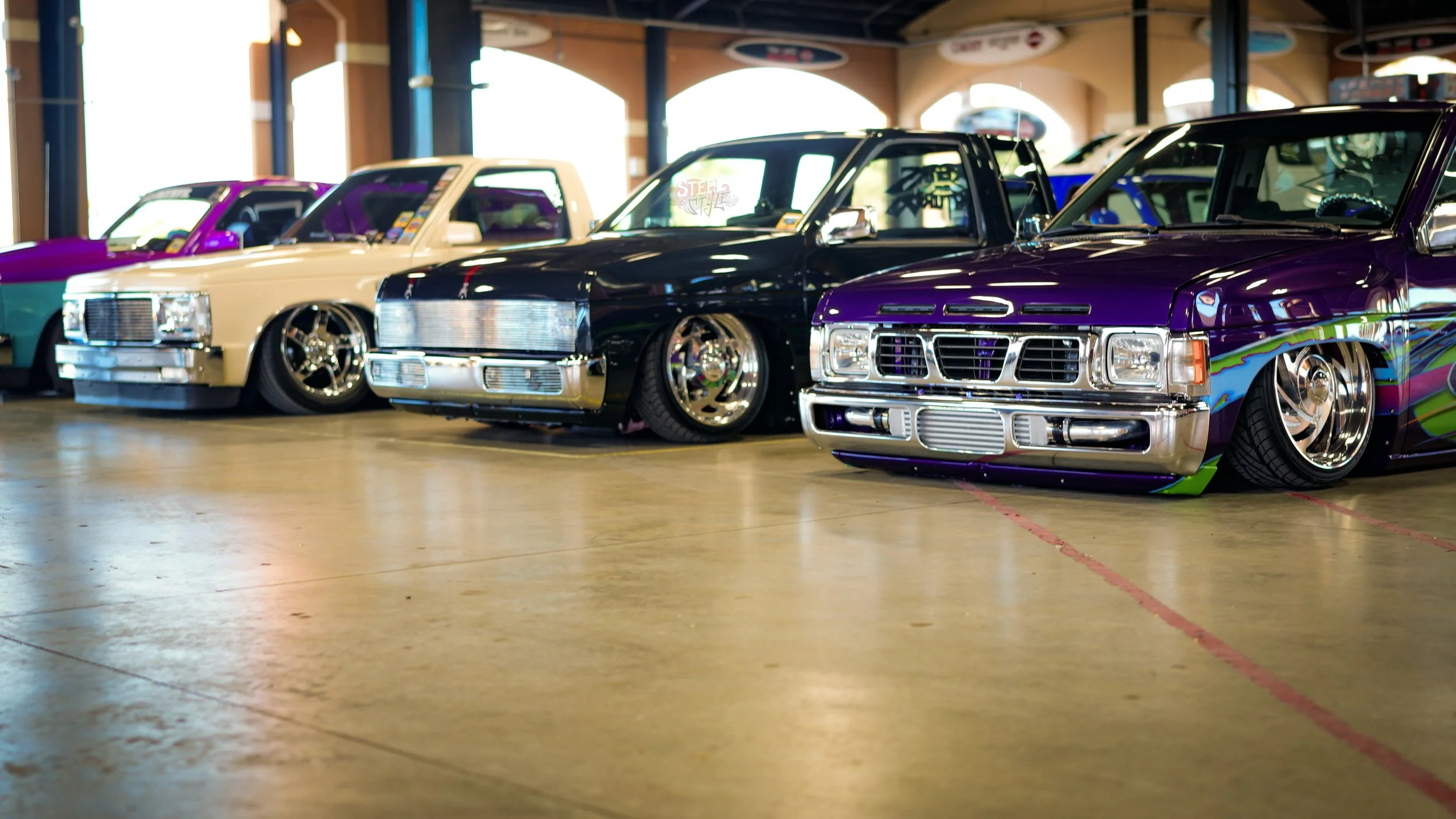 A row of customized lowrider cars with vibrant paint jobs at an indoor car show.