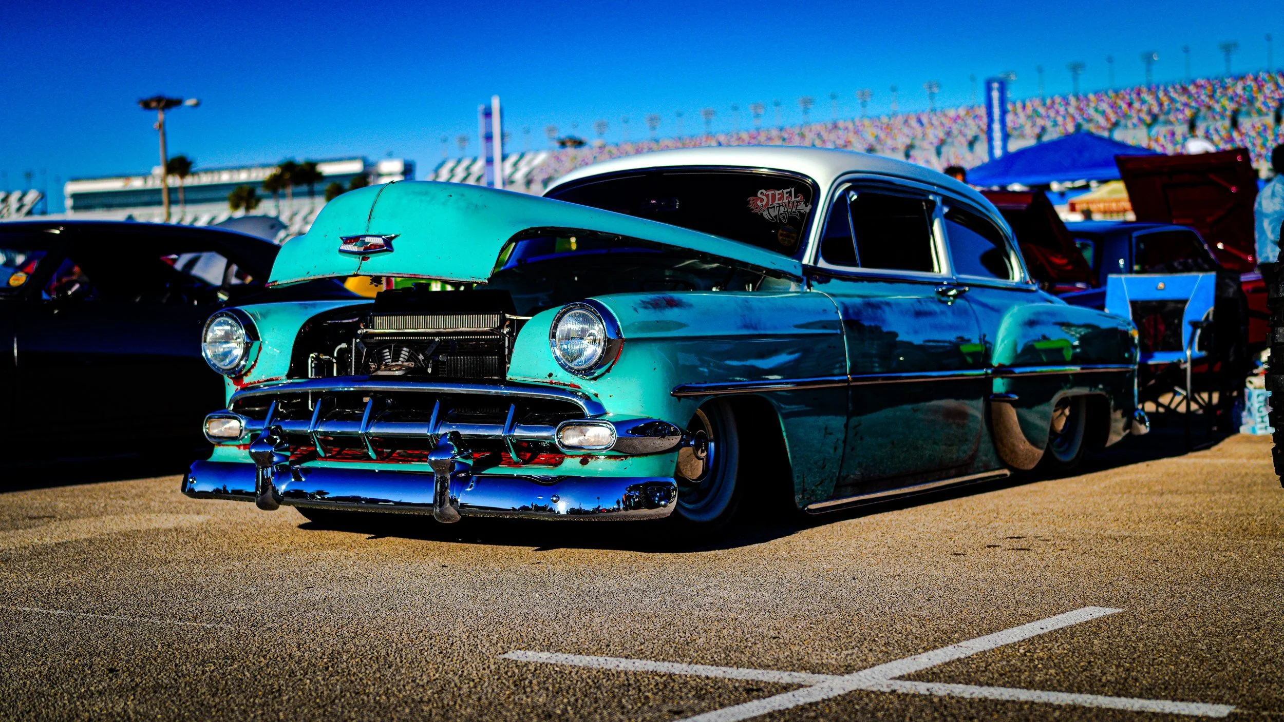 A vintage blue car with its hood open parked at a car show on a sunny day.