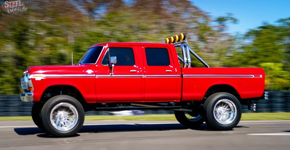 Red pickup truck driving on a road with trees in the background.