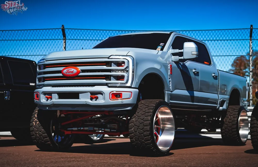 Custom lifted Ford truck with oversized wheels and off-road tires parked at an outdoor automotive event.