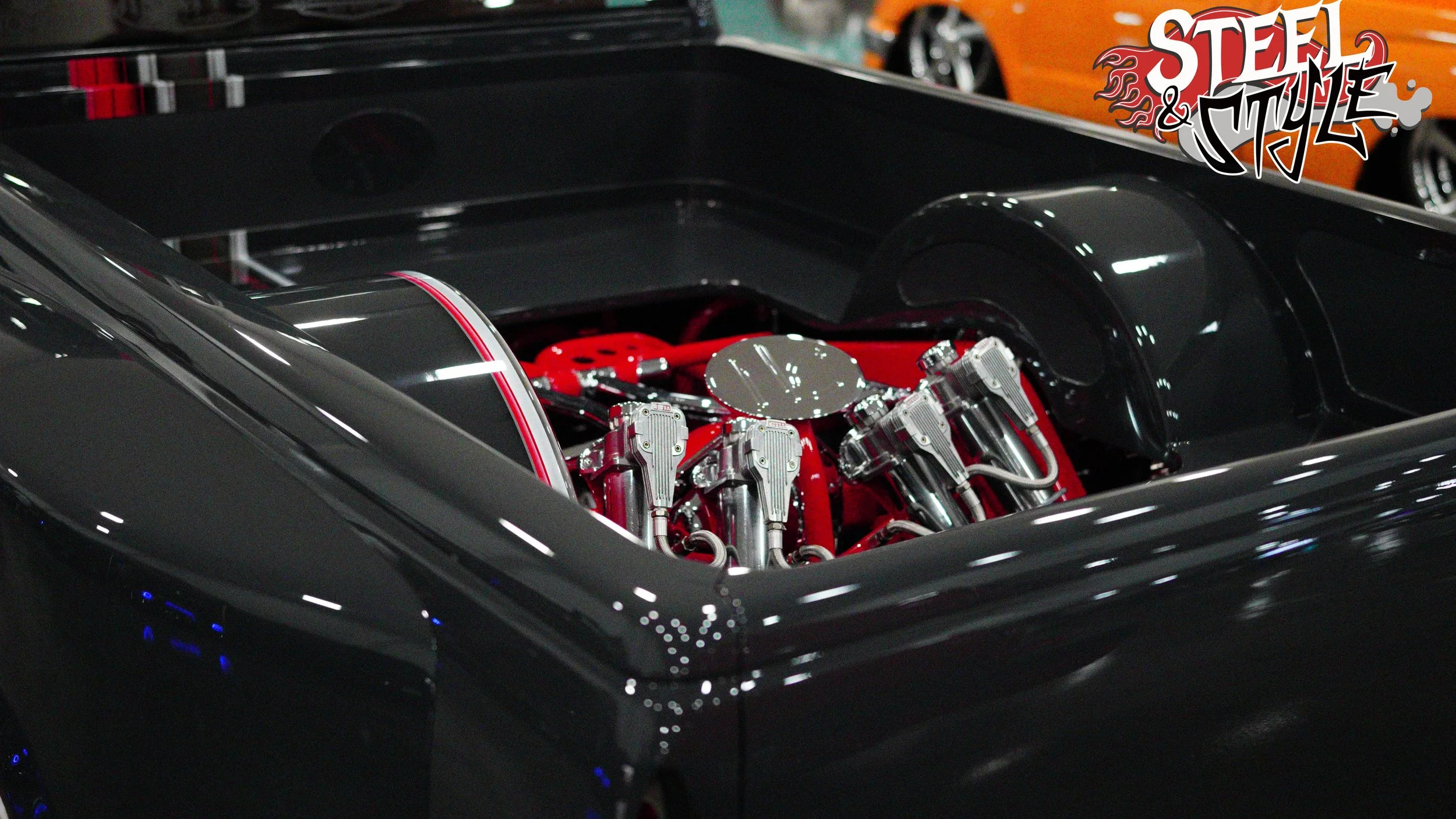 Close-up view of a high-performance car engine with chrome and red components in a glossy black engine bay, at an auto show.