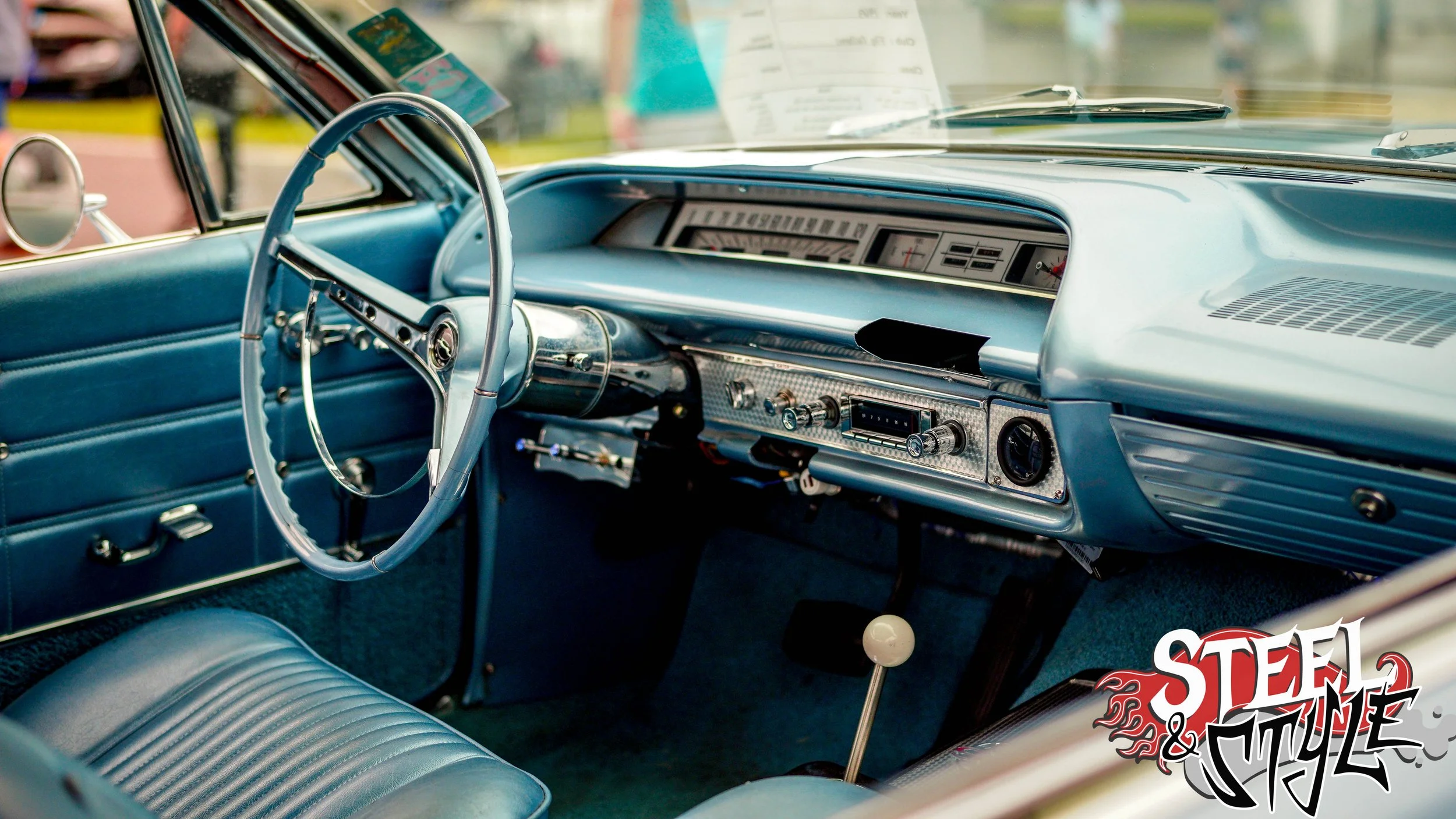Interior of a vintage blue car showing the dashboard, steering wheel, and front seat.