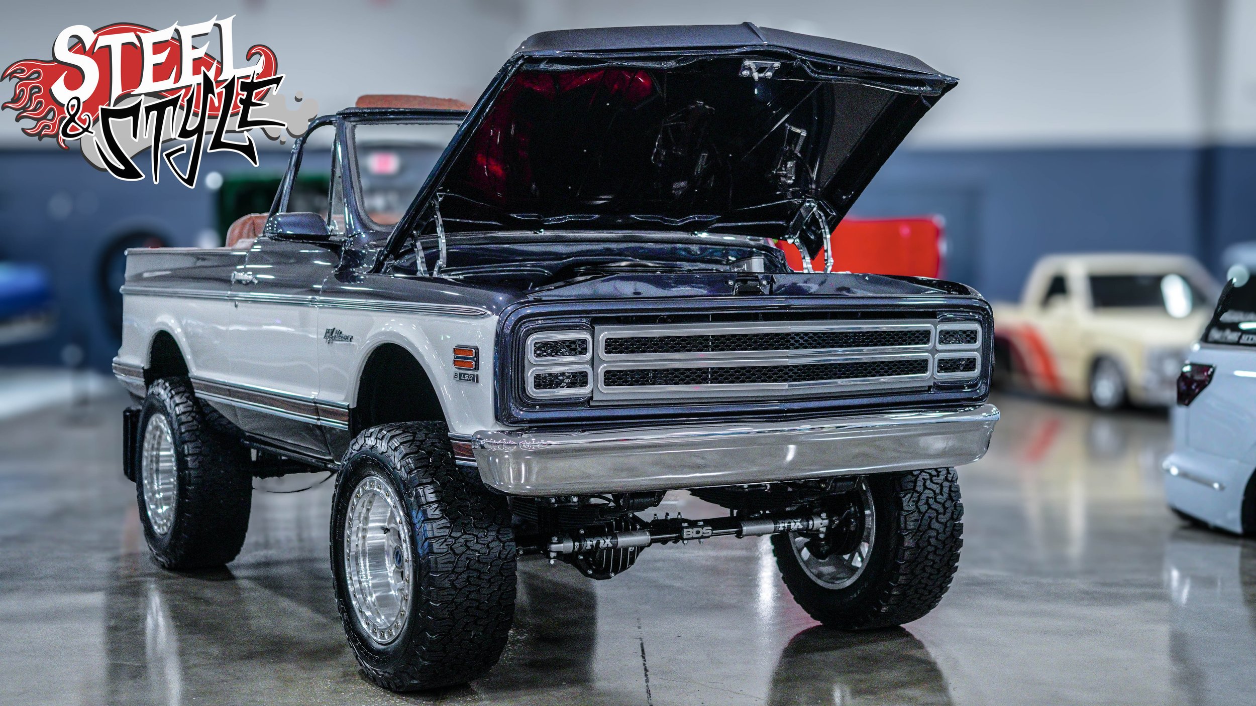 A detailed scale model of a classic Ford RANGER pickup truck with the hood open, displaying the engine bay. The truck is white with black accents, has large off-road tires, and is showcased indoors at a car show or exhibition.
