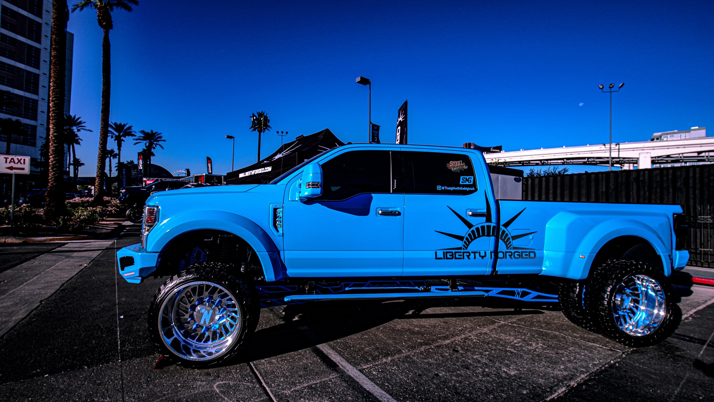 Blue custom lifted pickup truck with Liberty forged logo and chrome wheels parked in an outdoor lot.