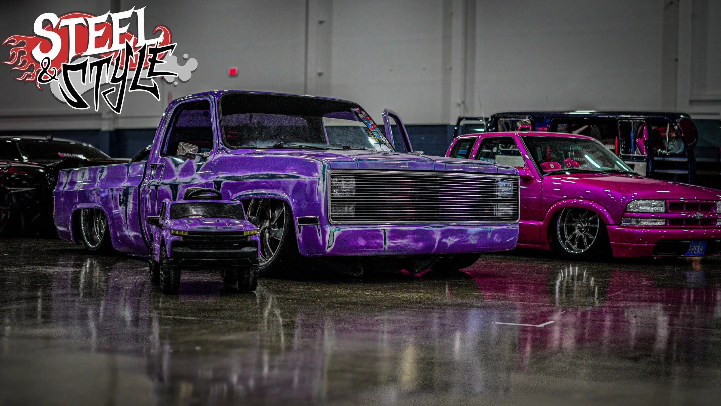 Multiple customized toy cars, including a purple pickup truck, a pink car, and a small purple sports car, are displayed indoors, with a "Steel & Style" logo in the top left corner.