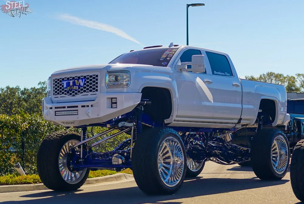 A large white lifted pickup truck with oversized wheels parked on the side of the road.