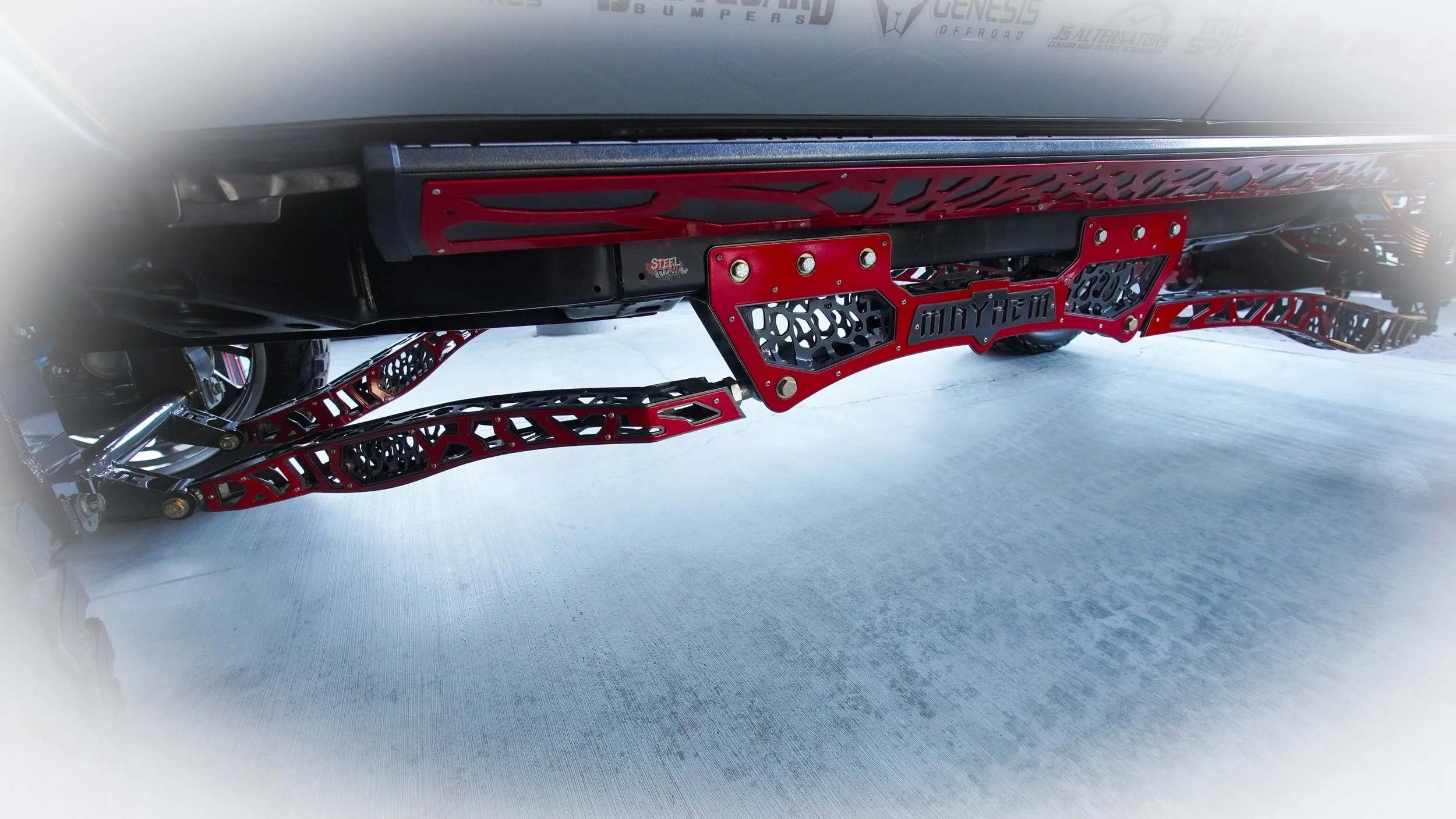 Close-up of a vehicle's side with red and black suspension components and custom decals, including 'Mayhem' branding.