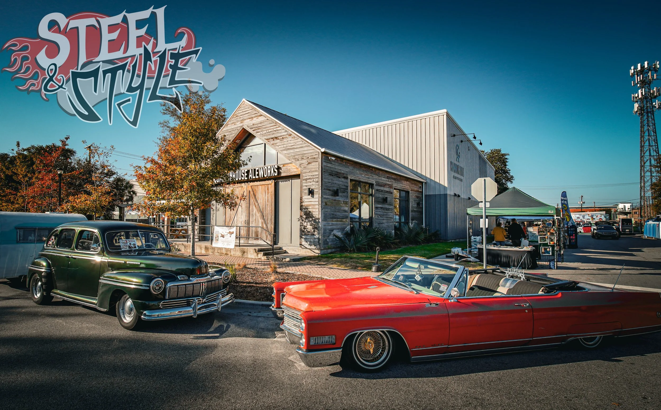 Vintage cars parked in front of the Steel & Thyme building with a market stall on the sidewalk, autumn trees, and a clear blue sky.