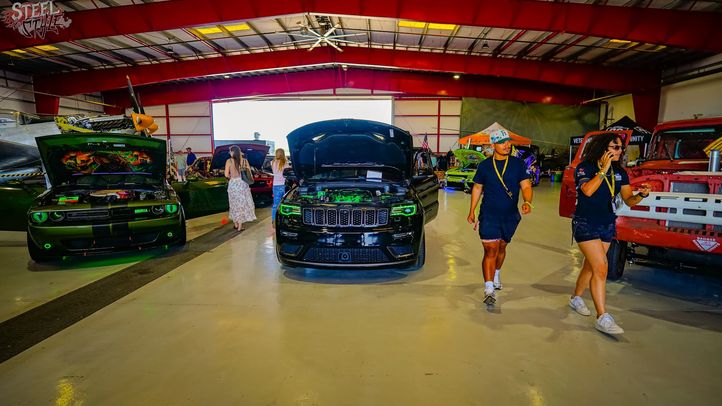 Indoor car show featuring various customized and vintage vehicles, with people viewing and walking around the exhibits.