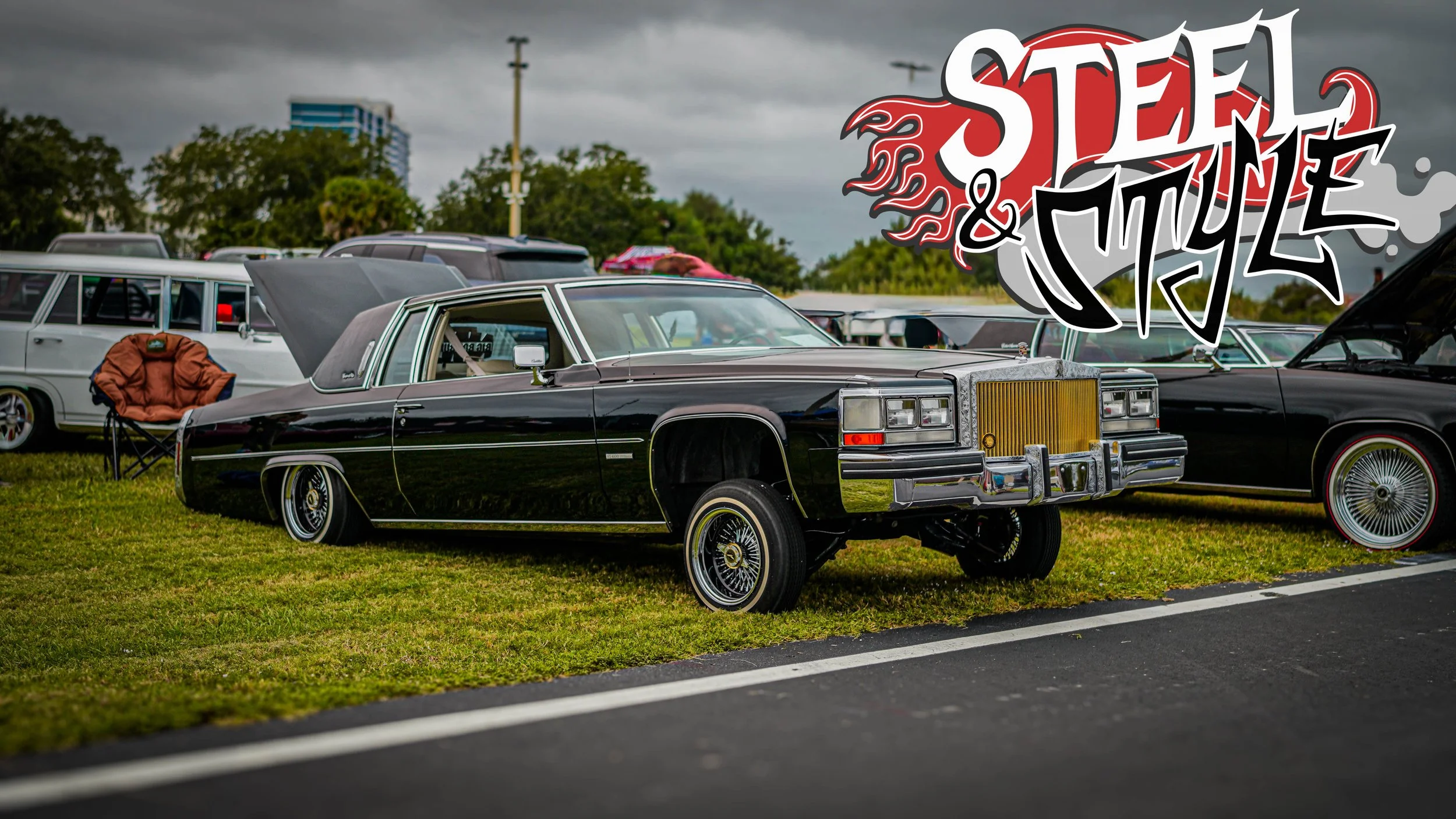 A black vintage Cadillac car at a car show with a graffiti-style "Stell & Style" logo.