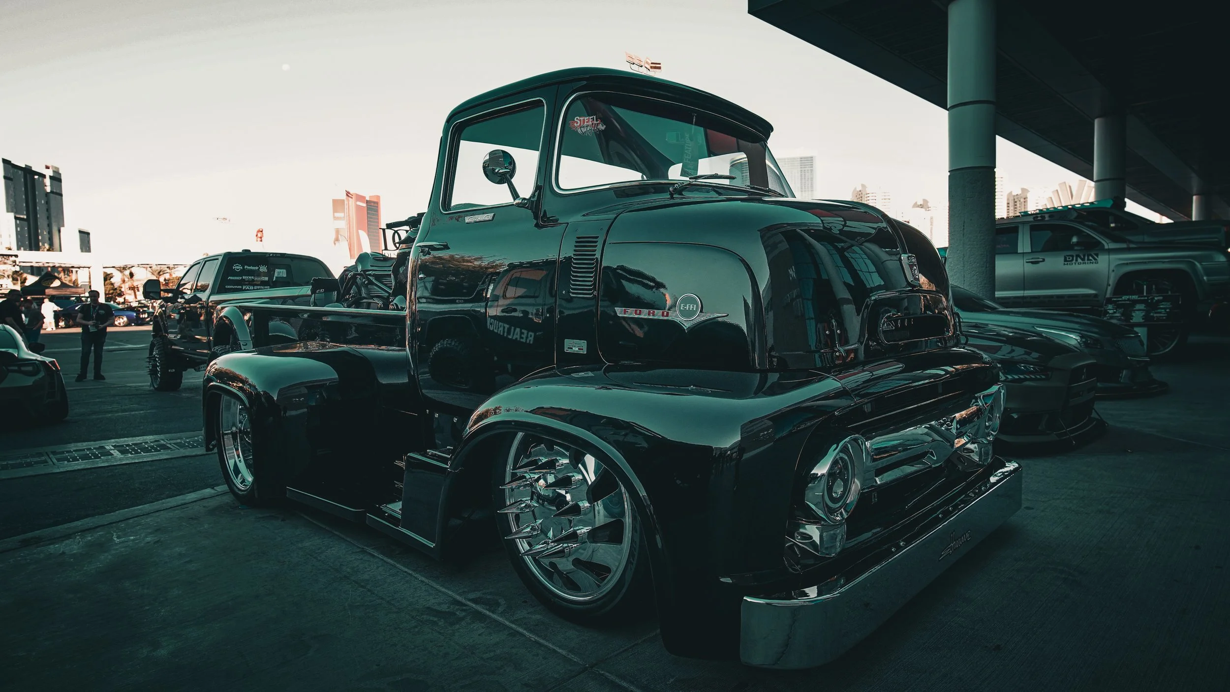 A customized vintage Ford pickup truck with a highly polished black exterior and unique chrome wheels, displayed at a car show.
