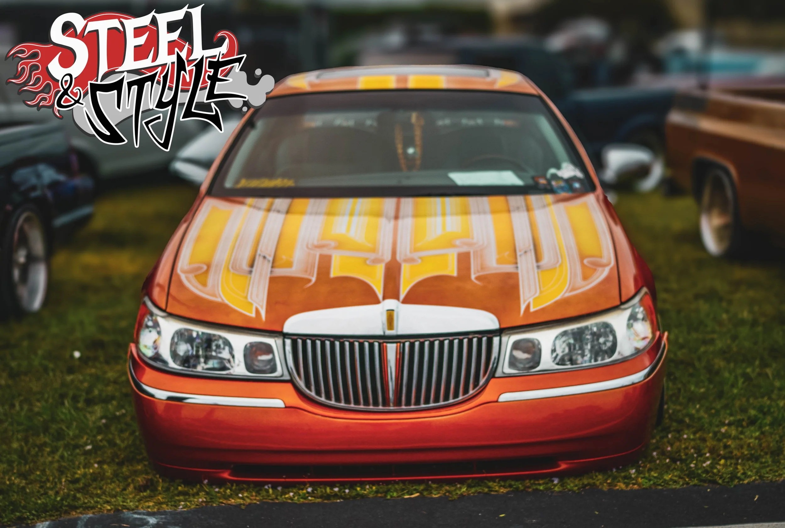 Red car with yellow and white graffiti-style artwork on the hood, parked on grass among other vehicles, with a 'Steel & Muzzle' graffiti graphic overlay in the top left corner.