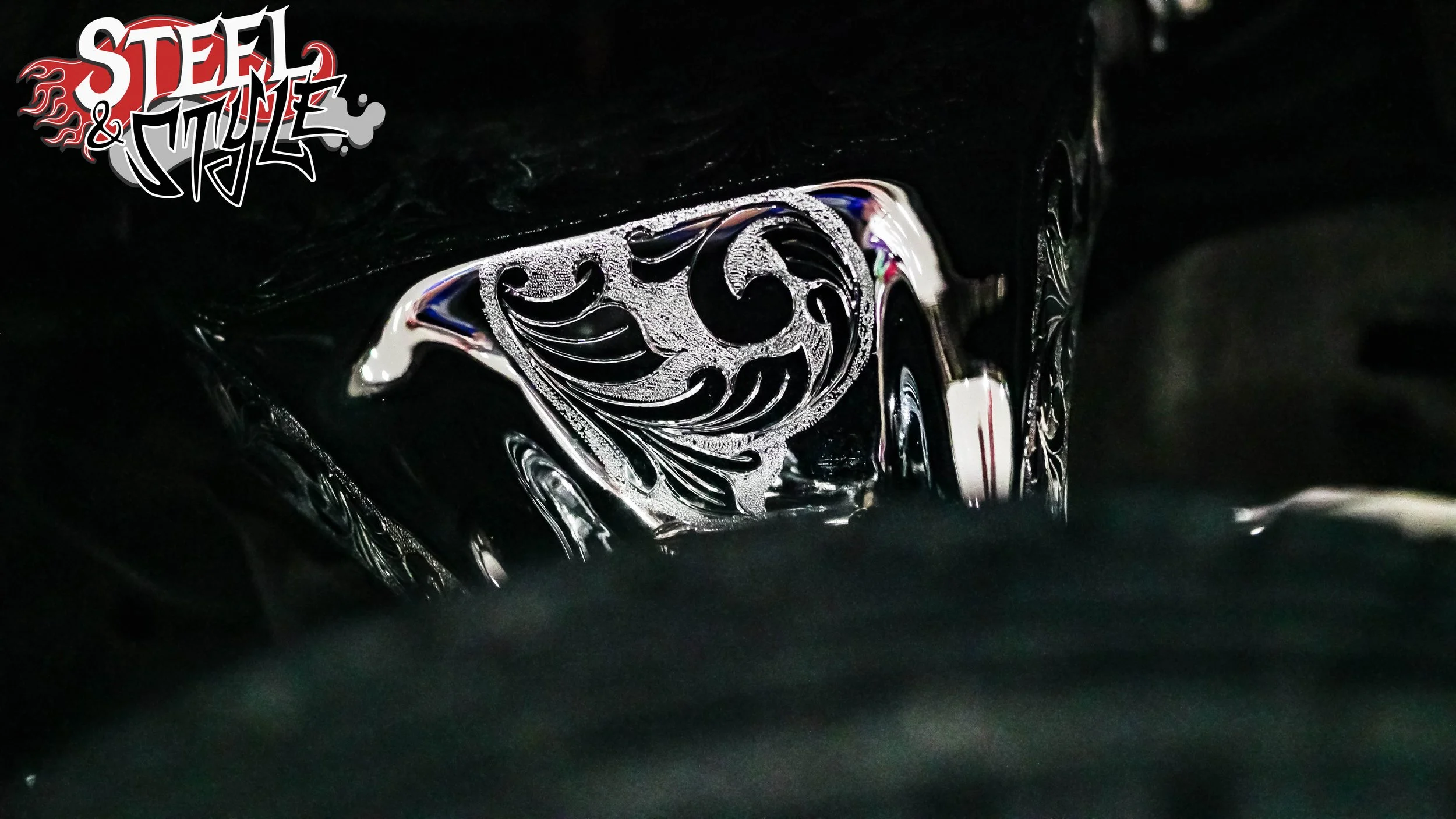 Close-up of an intricately designed silver badge or emblem on a black surface, with a logo reading 'Steel & Style' in the top left corner.
