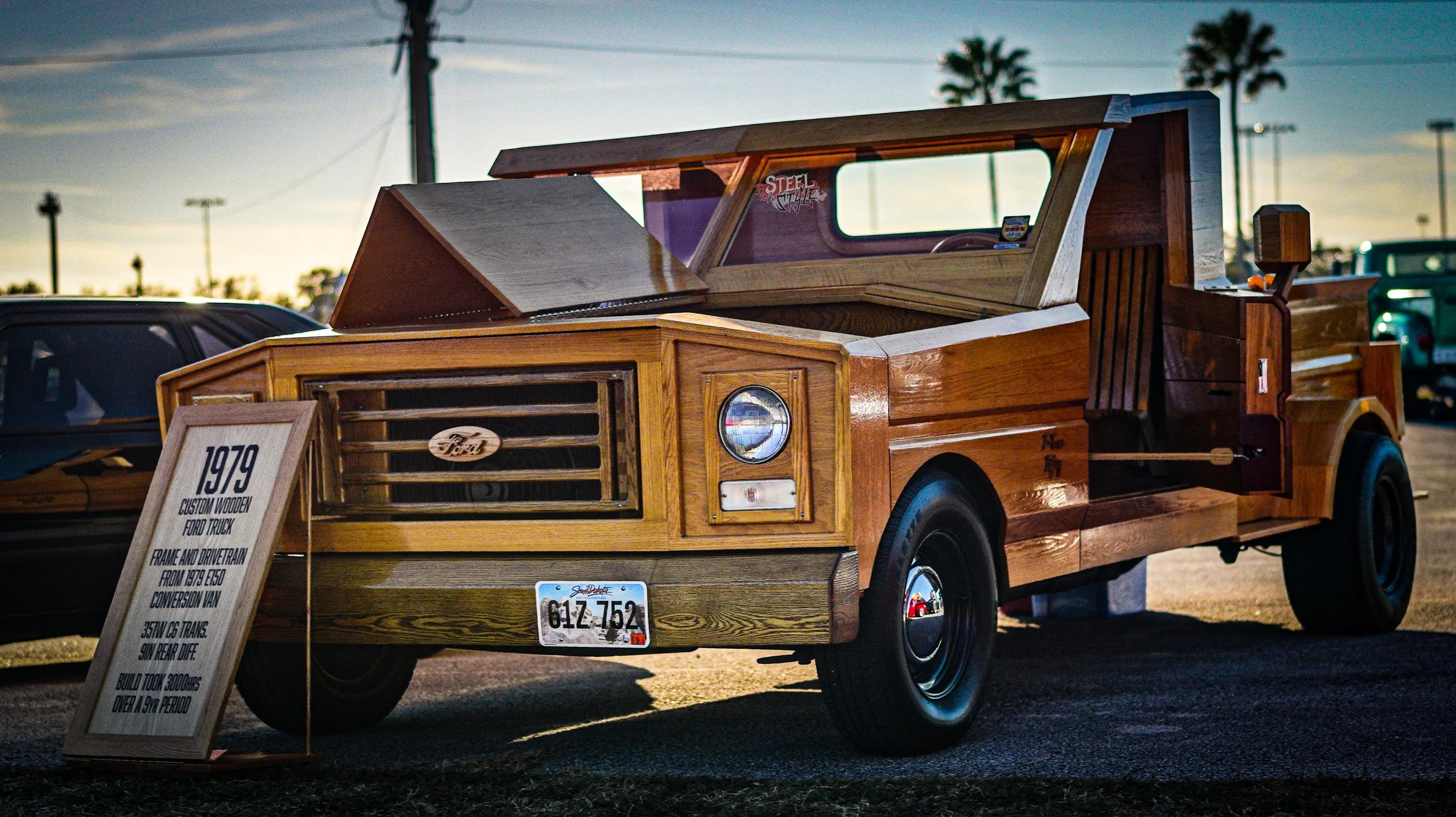 1980s custom wooden Ford truck displayed at a car show, with a sign describing its history and modifications.