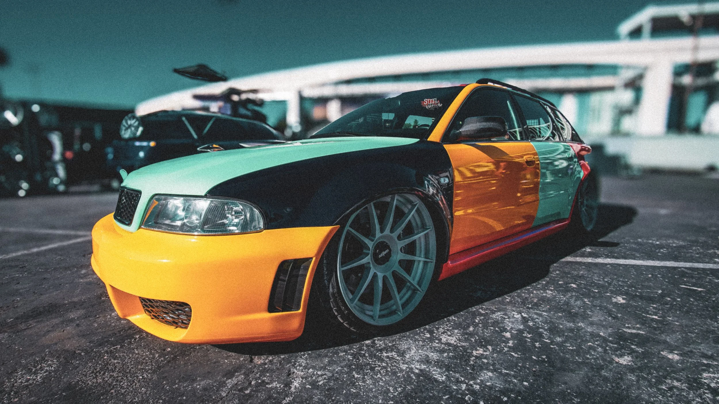 A low-angle view of a customized sports car featuring a tricolor paint job with yellow, black, and green sections parked in a lot at night.