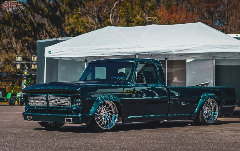 A dark green custom lowered pickup truck with large aftermarket wheels parked outdoors.