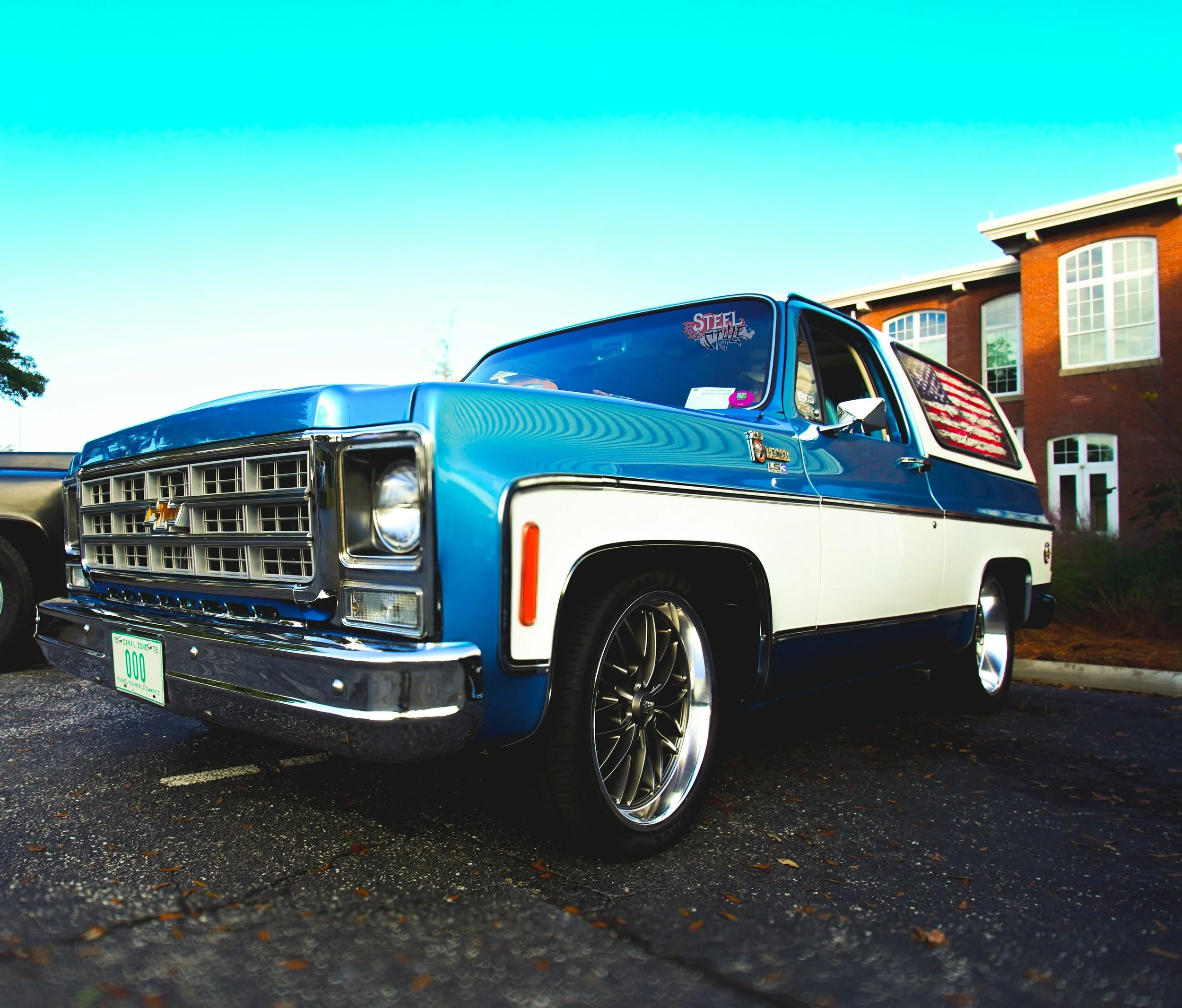 A vintage blue and white Chevrolet SUV parked outdoors in a parking lot with a brick building and trees in the background.
