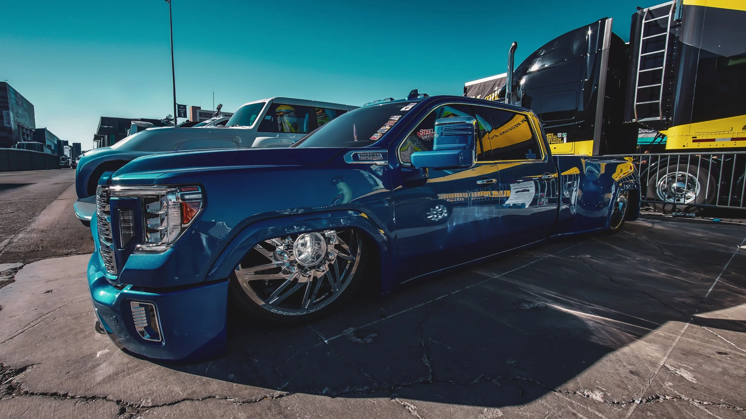 Blue customized pickup truck with lowered suspension, large rims, parked outdoors under clear blue sky.