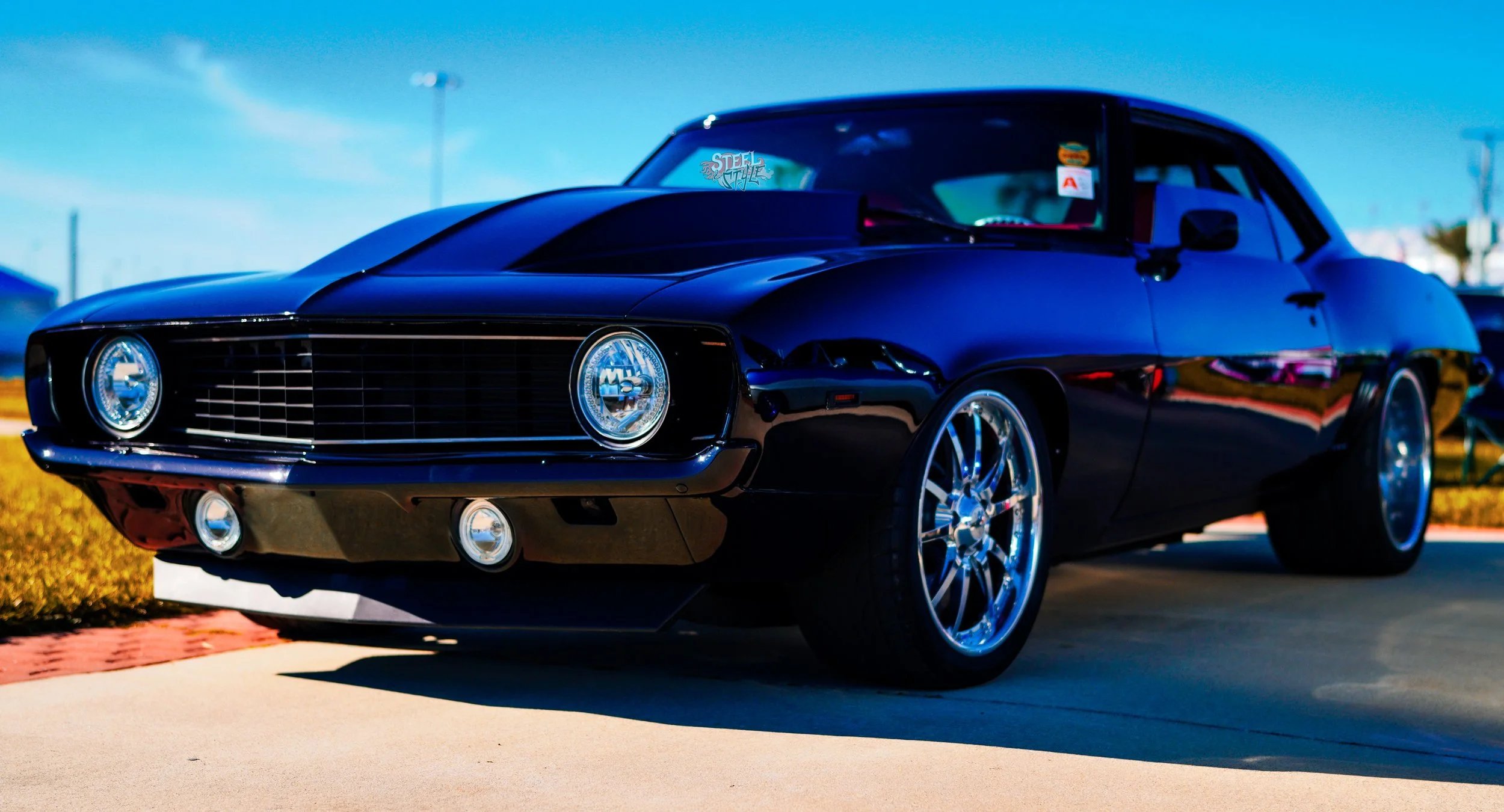 Black vintage muscle car parked on pavement with clear blue sky in the background.