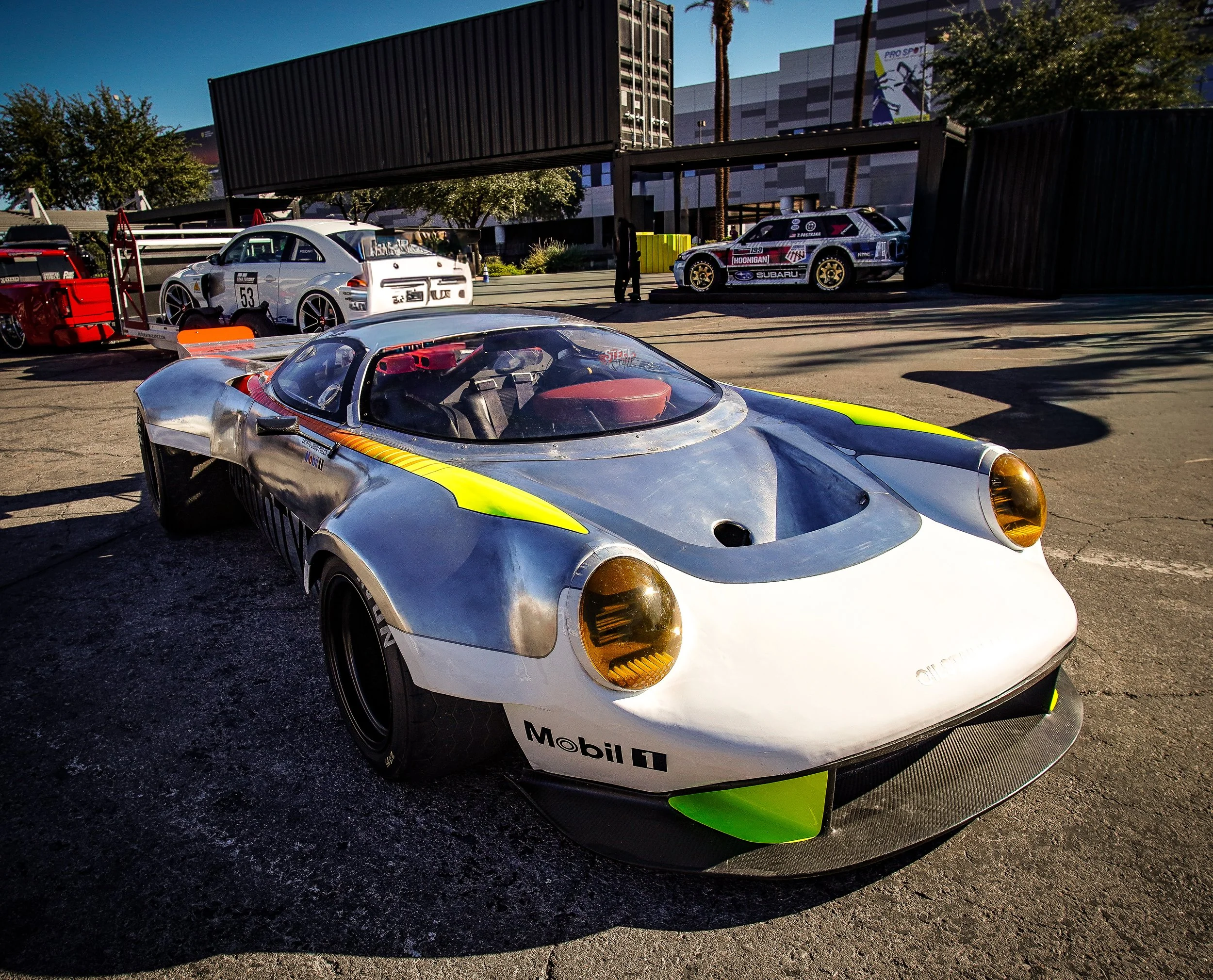 A vintage racing car in a garage with other racing cars in the background under clear sky.