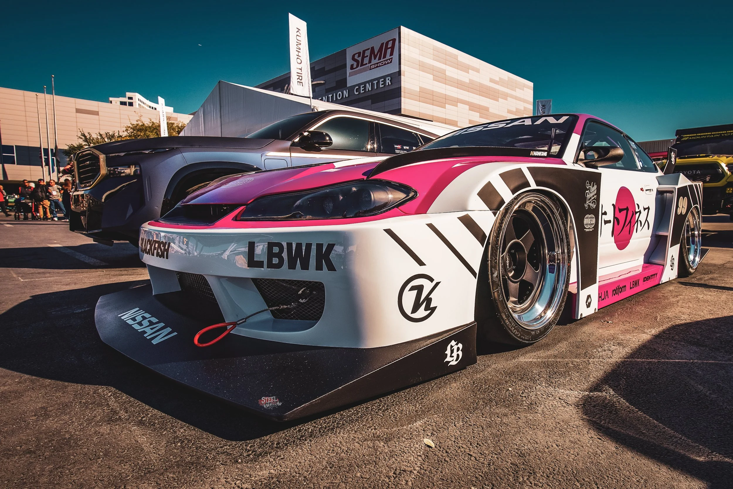 A race car with a pink, white, and black design at an outdoor car show.